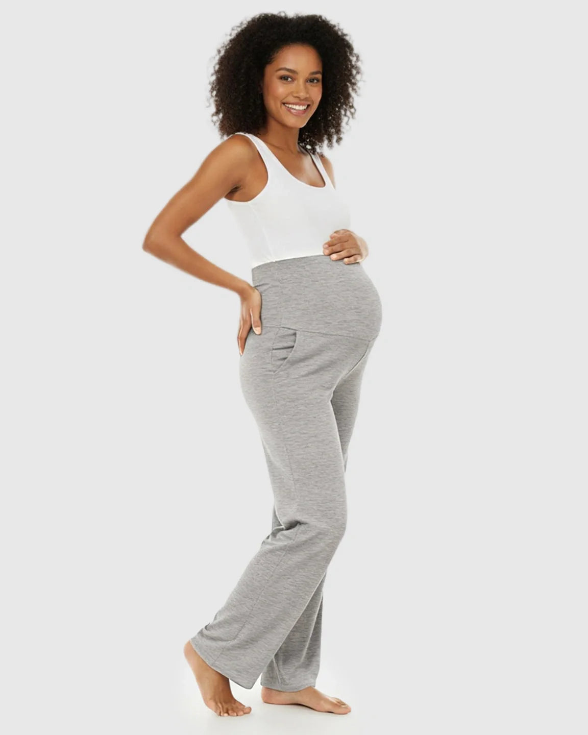Smiling pregnant woman in light gray wide-leg maternity lounge pants with a foldable waistband and side pockets.