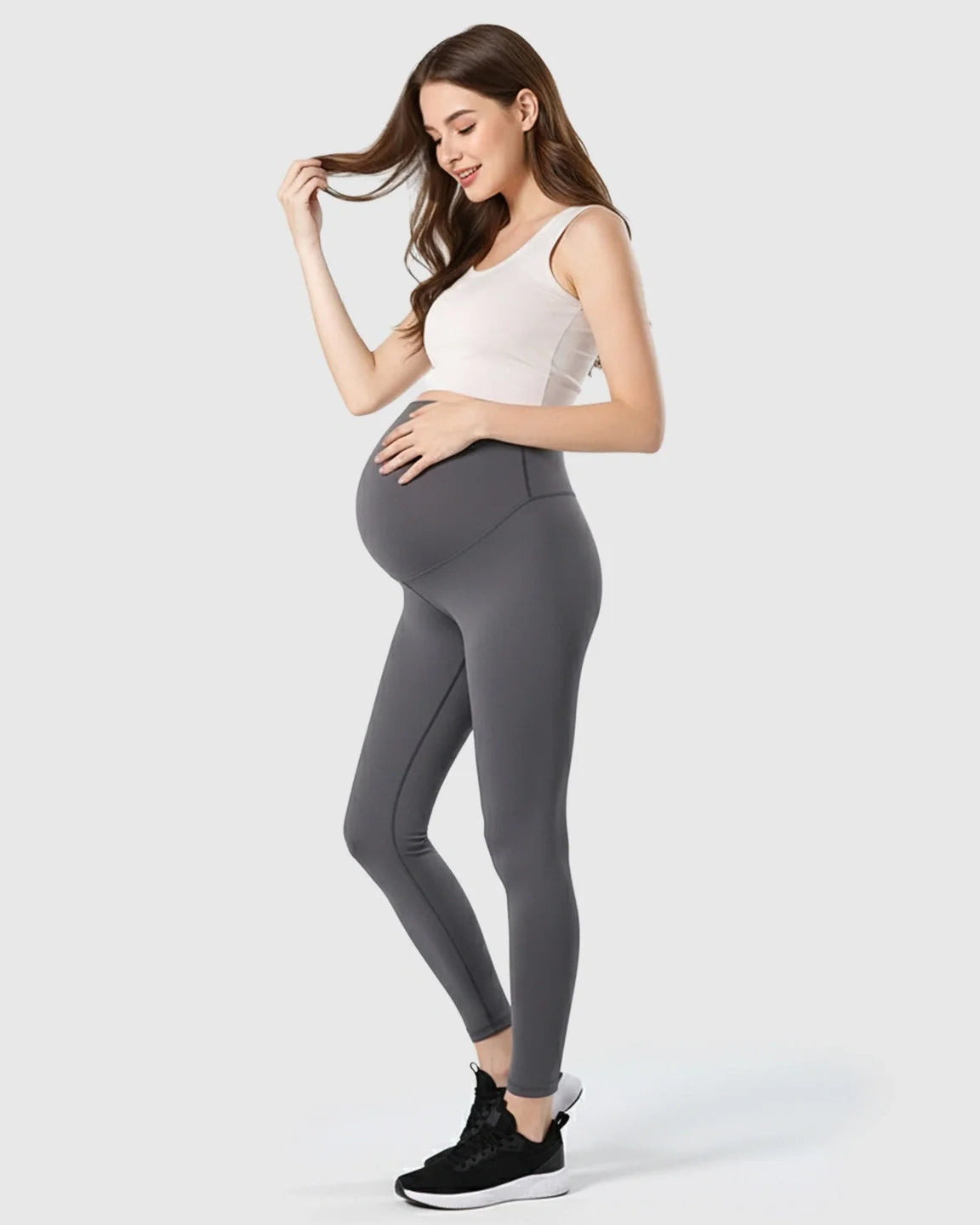 Pregnant woman in dark gray double-layer belly support maternity leggings and a white tank top.