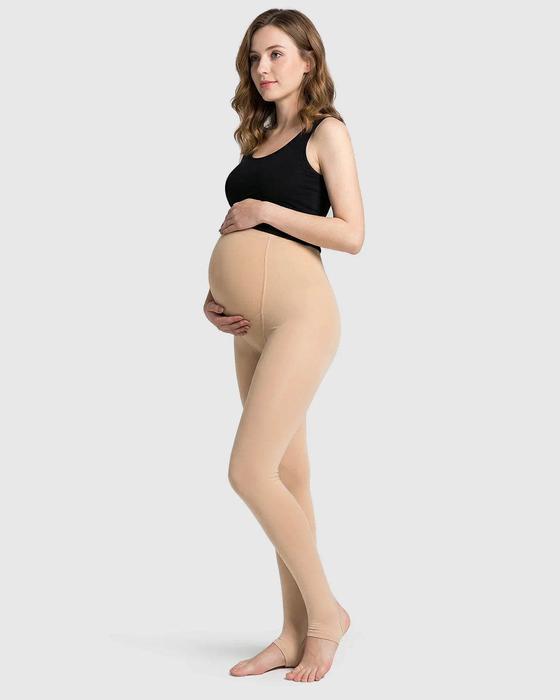 Pregnant woman modeling nude fleece-lined over-bump maternity leggings with stirrup design.