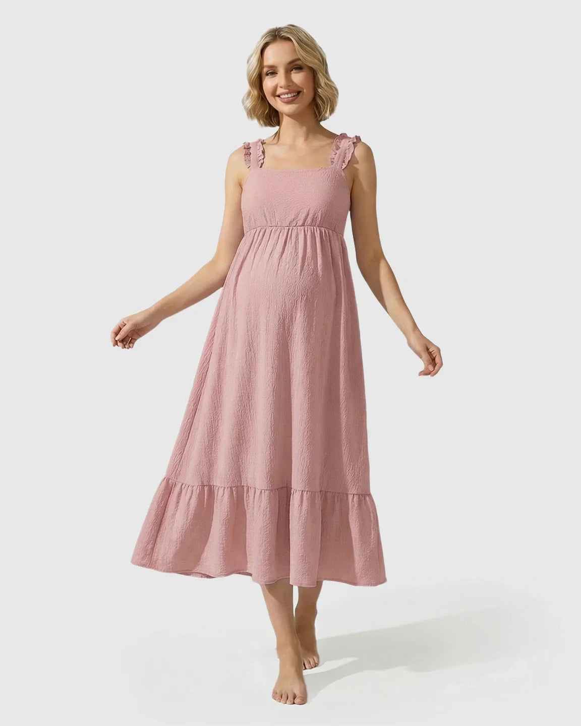 Smiling pregnant woman in a pink ruffled strap maternity maxi dress with a tiered skirt.