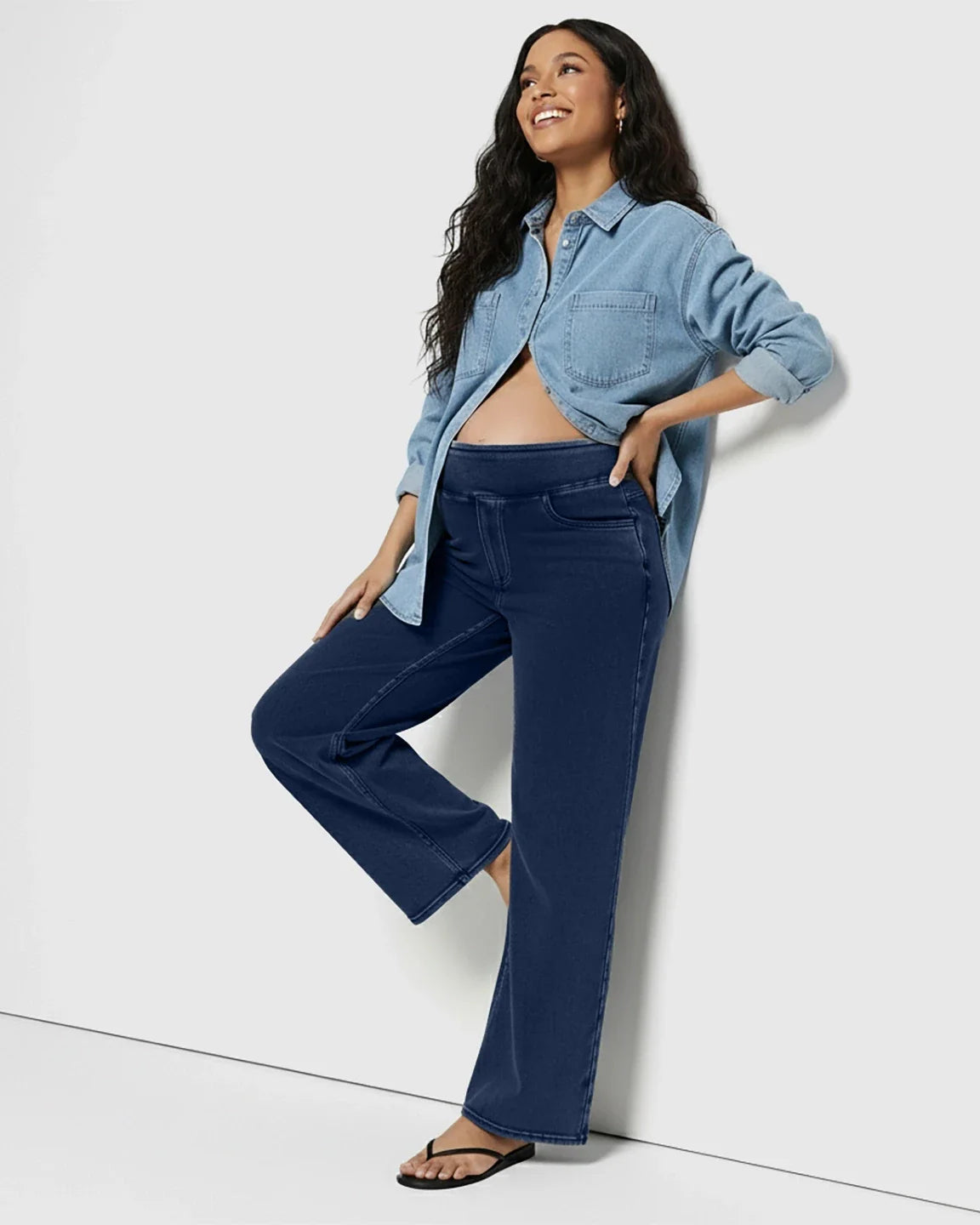 Smiling pregnant woman in navy high-waist wide-leg maternity denim jeans and a light blue chambray shirt.