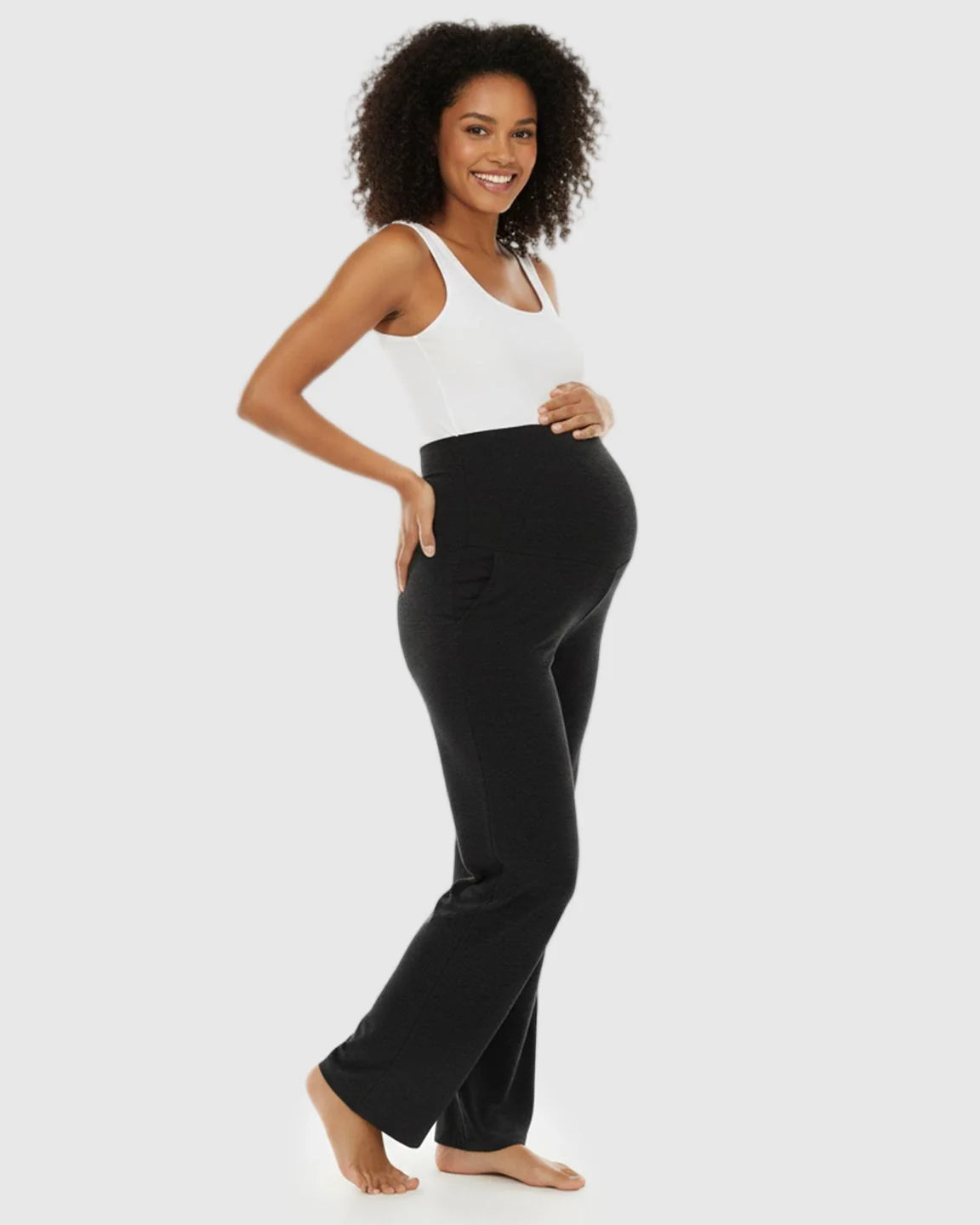 Smiling pregnant woman in charcoal wide-leg maternity lounge pants with a foldable waistband and side pockets.
