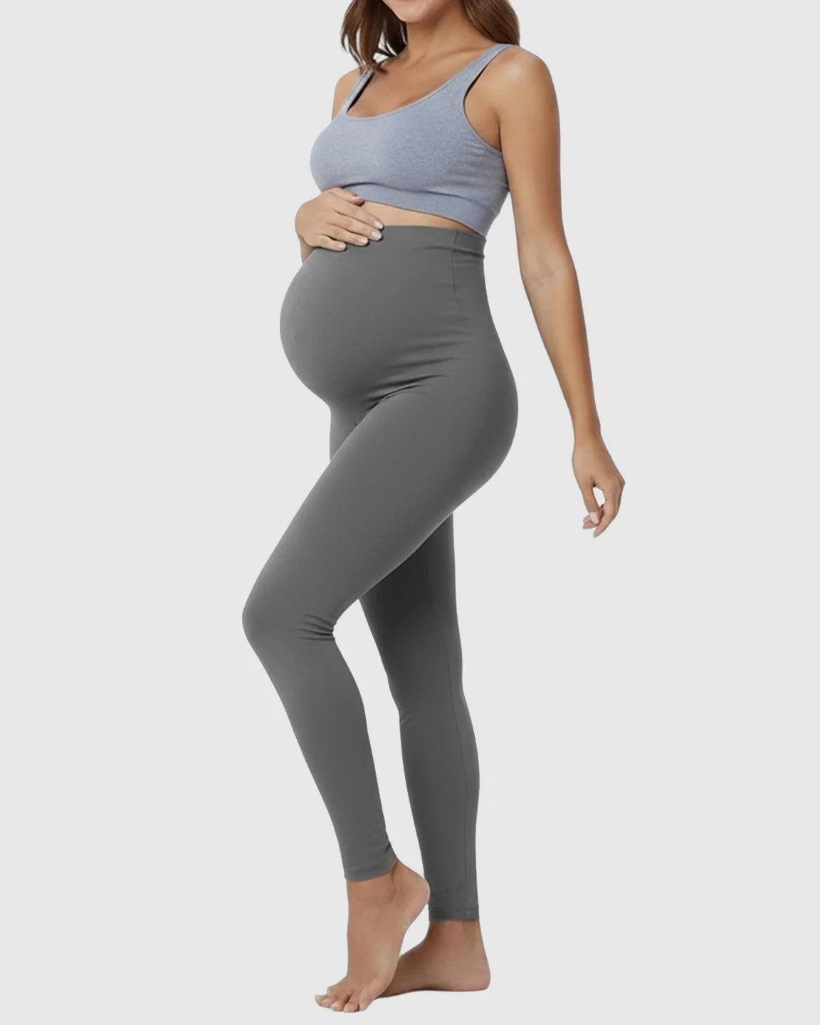 Pregnant woman in full-length, seamless, high-waist grey maternity support leggings, gently cradling her belly.