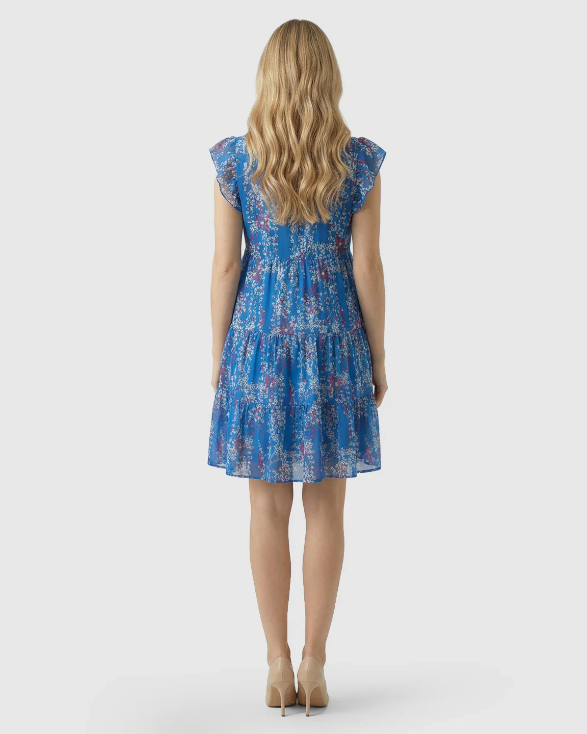 Blonde woman from behind in a blue floral chiffon V-neck A-line maternity dress with tiered skirt.