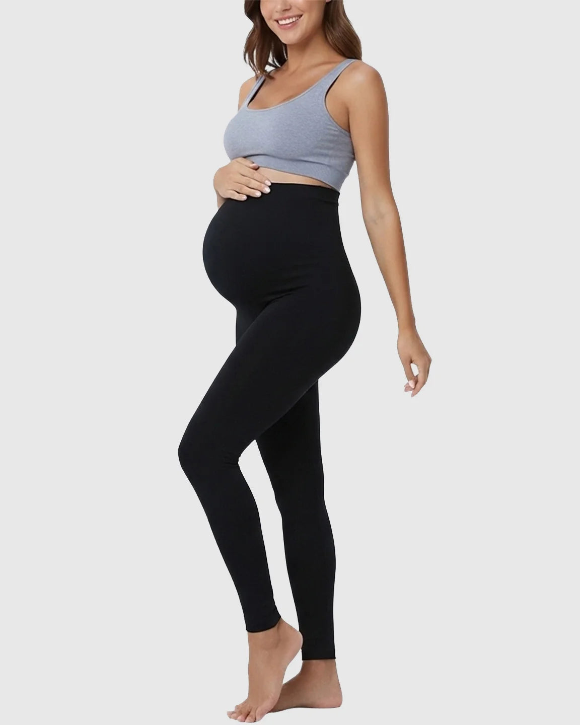 Smiling pregnant woman wearing black high-waist maternity support leggings and a gray crop top.