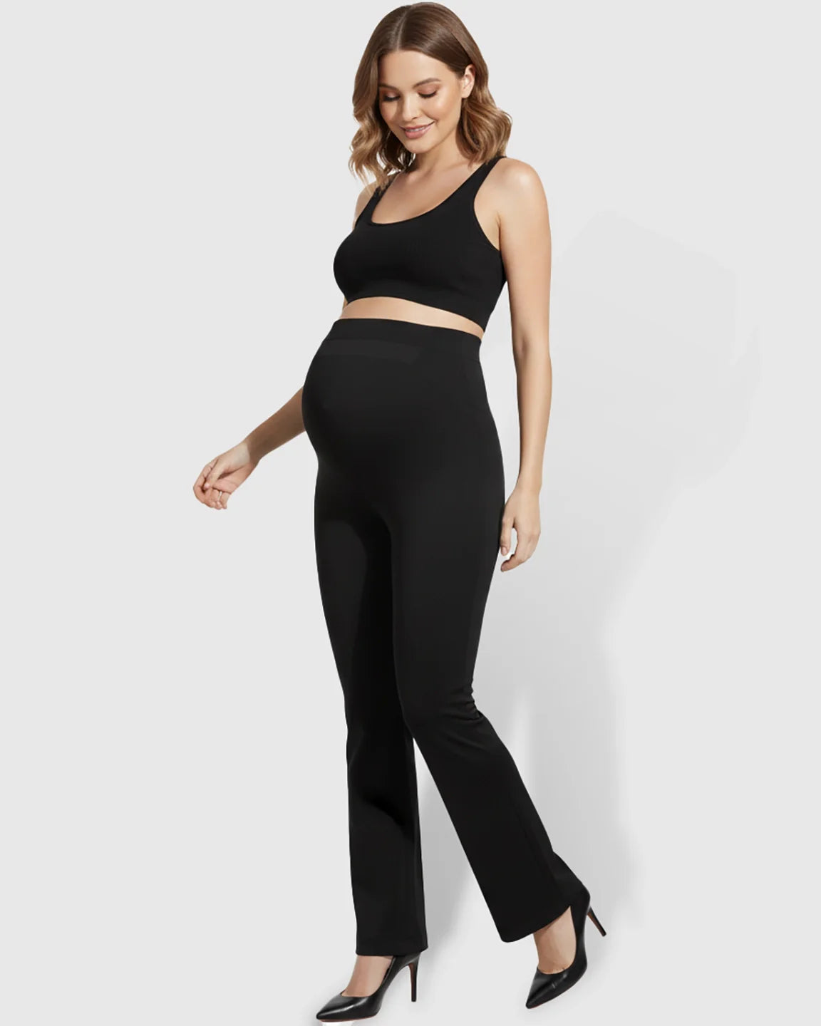 Smiling pregnant woman in black over-belly bootcut maternity pants and a matching crop top.