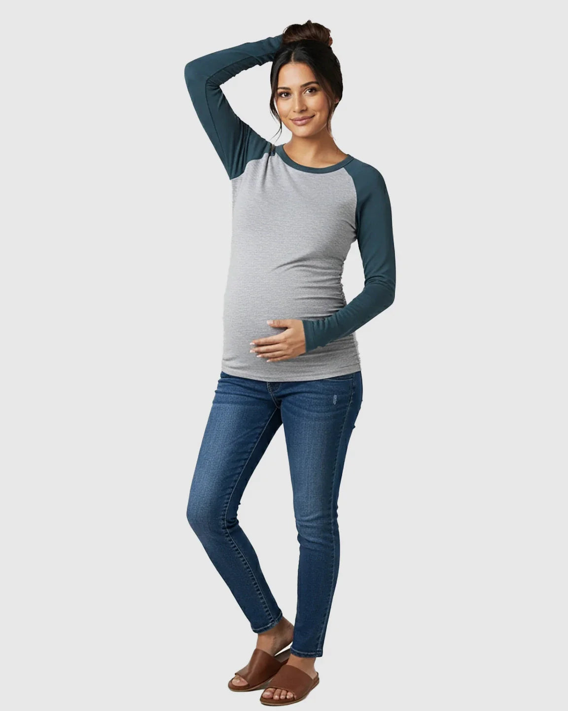 Maternity model in a gray and teal raglan sleeve stretch-fit long-sleeve top with side ruching, blue jeans, and brown mules.