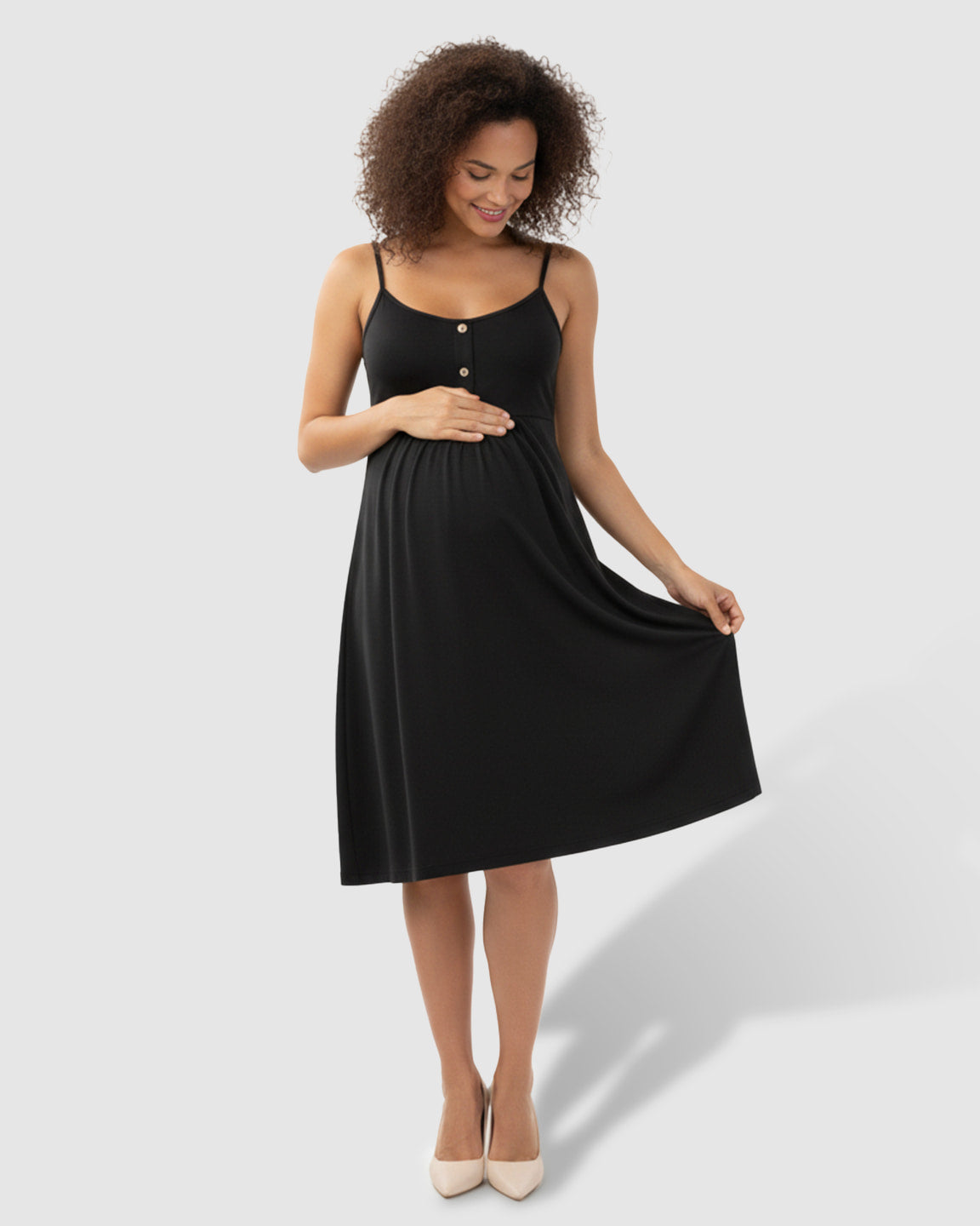 Smiling pregnant woman in a black thin-strap A-line maternity midi dress with front buttons, holding her belly.