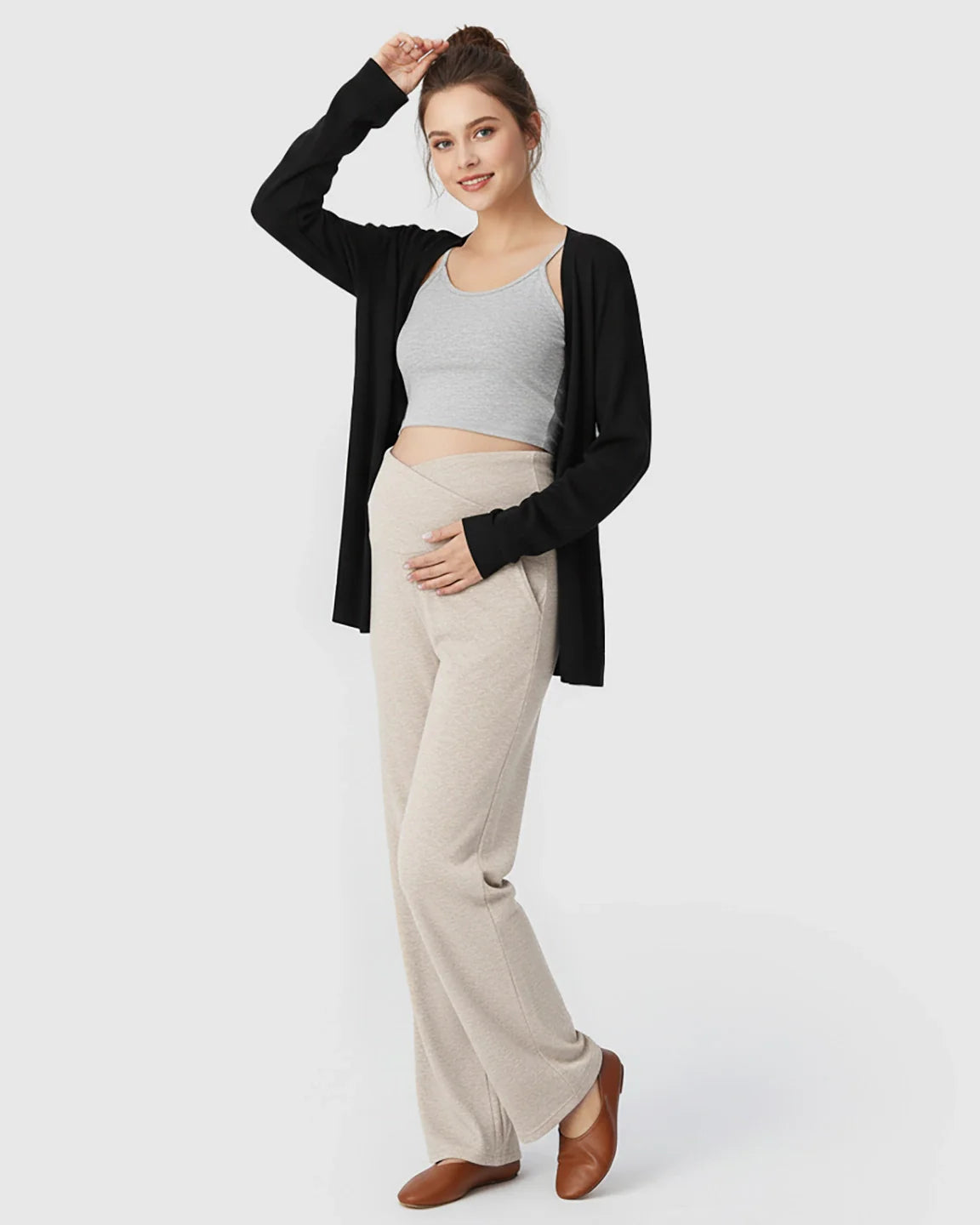 Pregnant woman in beige crossover waist wide-leg maternity lounge pants, grey crop top, and black cardigan.