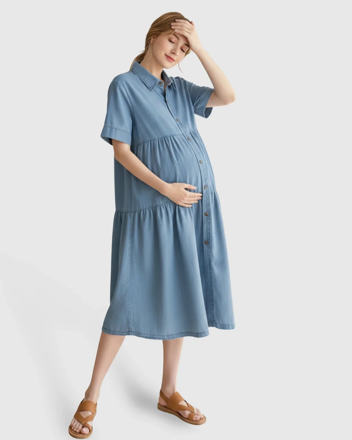 Pregnant woman in a light blue tiered denim maternity midi dress with button-front and short sleeves.