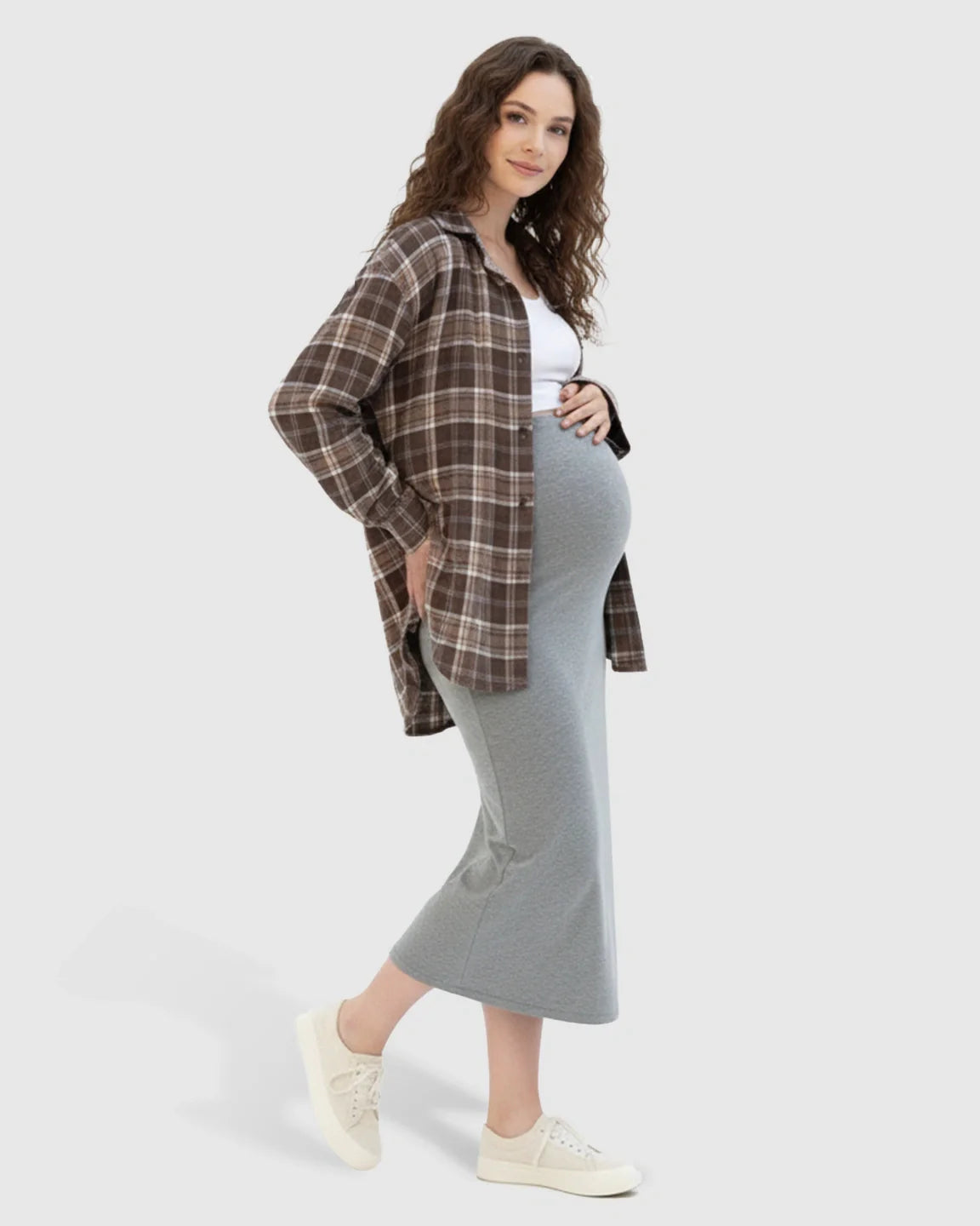 Pregnant woman in a light grey midi maternity skirt, white top, and brown plaid shirt.