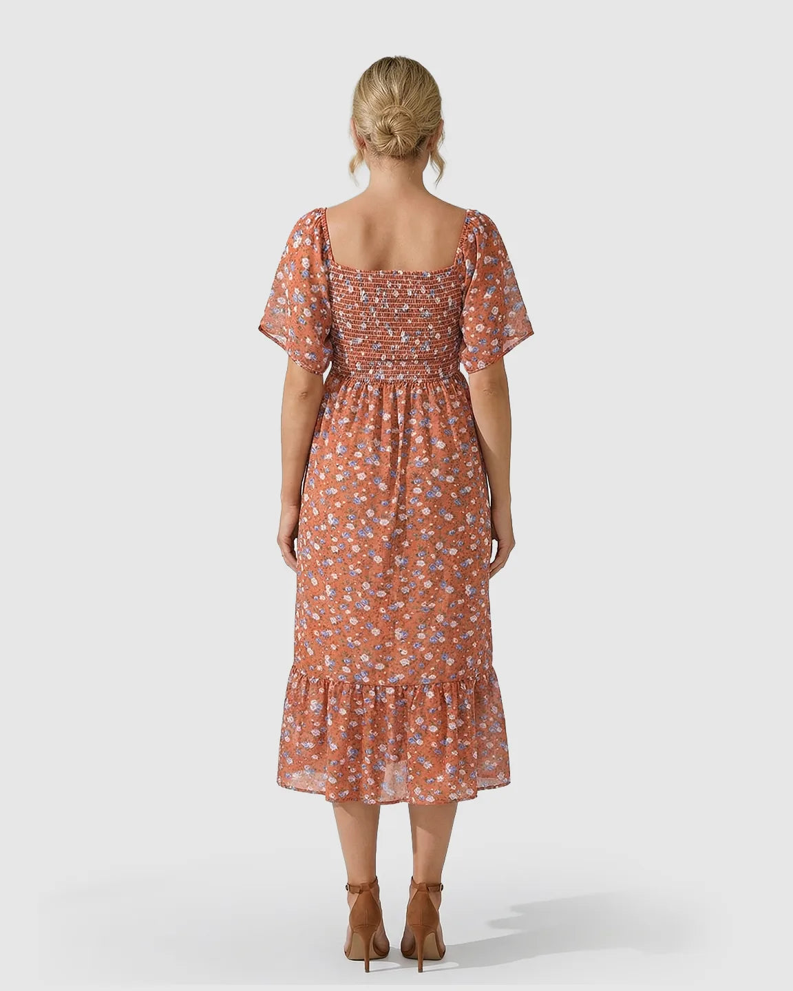 Back view of a pregnant woman in a rust orange floral flutter-sleeve smocked maternity midi dress.