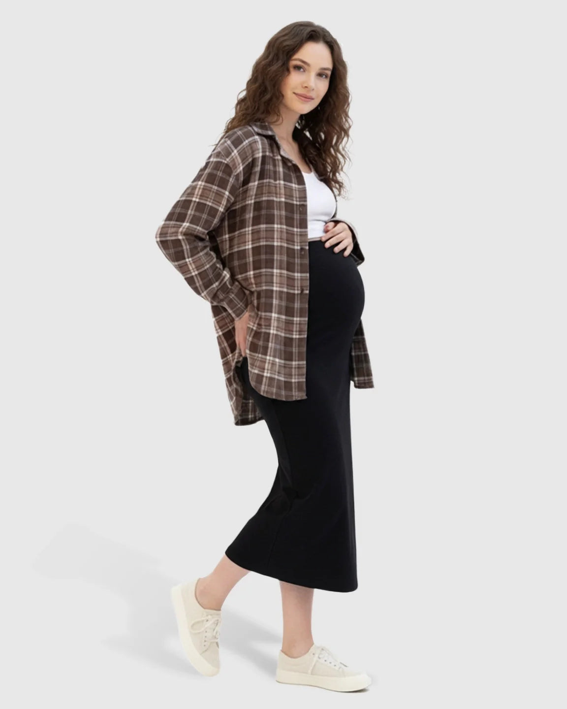 Pregnant woman in a black midi skirt, white top, and brown plaid shirt, showcasing the comfortable fit.