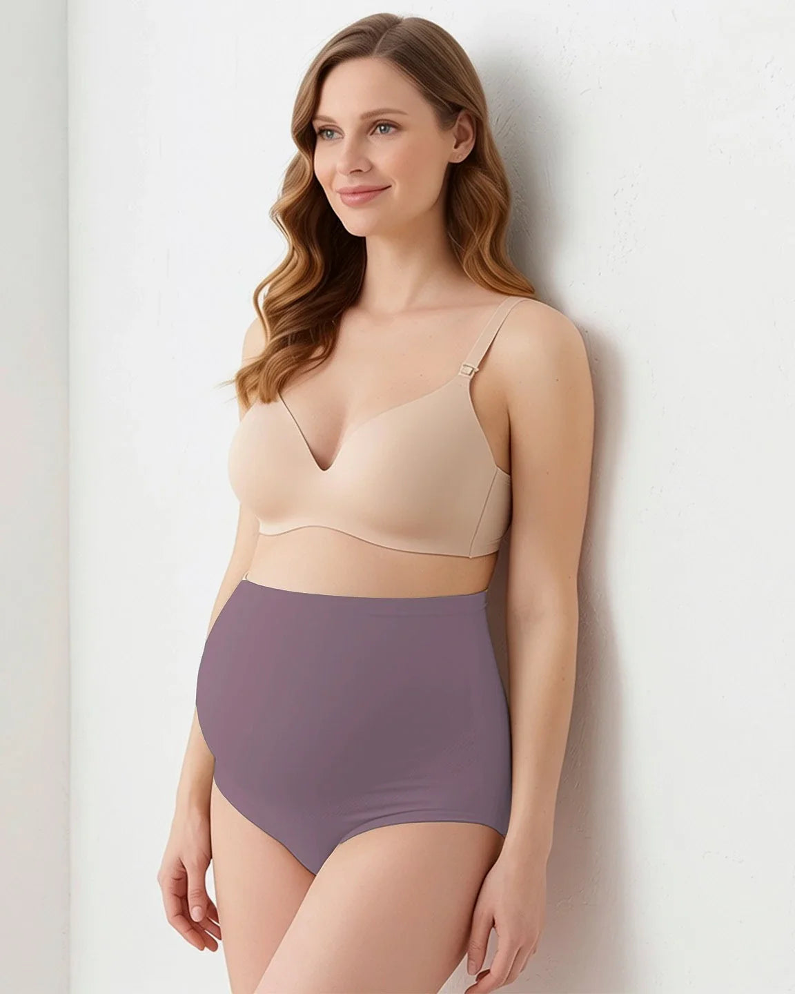 Smiling pregnant woman models high-waist, full-coverage seamless maternity briefs in plum, paired with a nude bra.