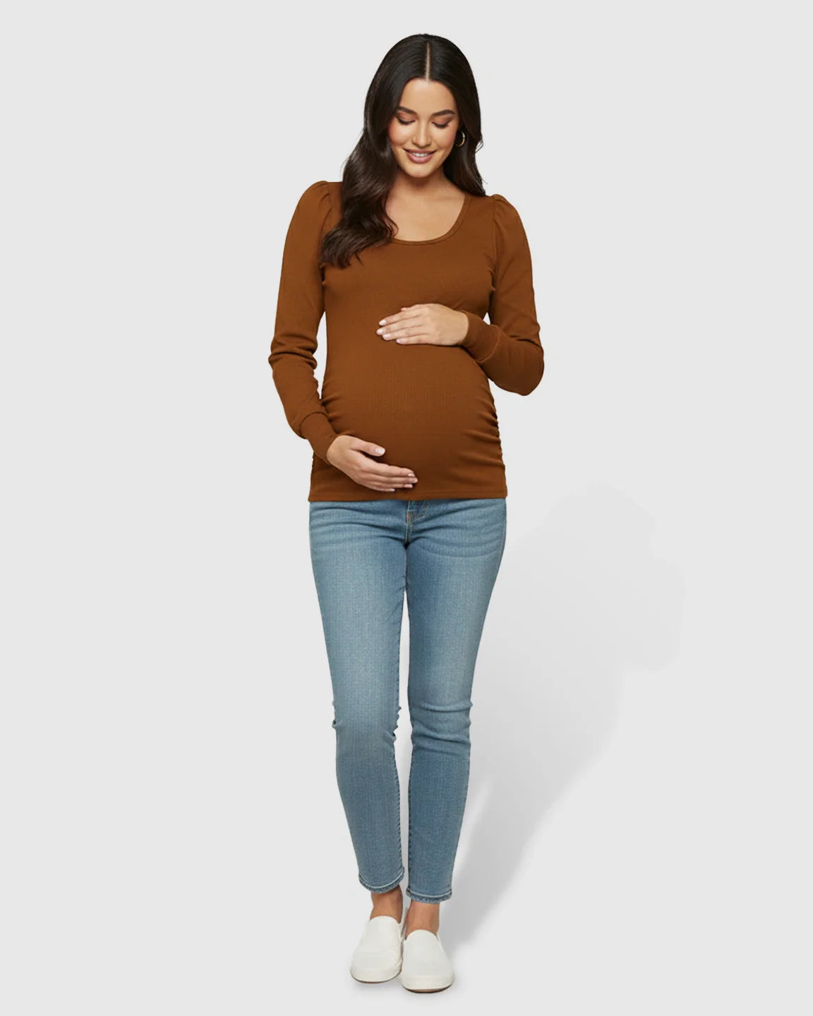 Pregnant woman in a warm brown long-sleeve ruched maternity top with a round neck and light wash jeans.