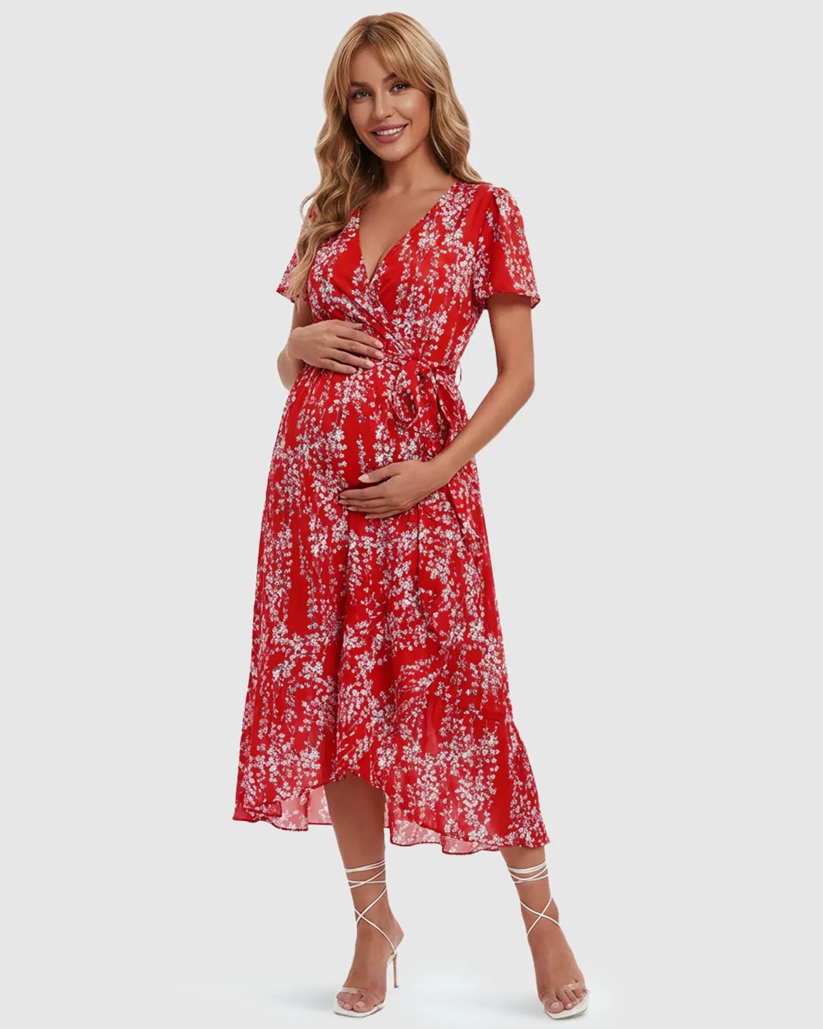 Smiling pregnant woman in a red floral V-neck ruffled hem maternity midi dress, holding her bump.