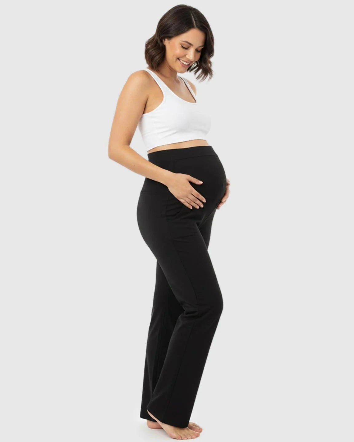 Smiling pregnant woman in black stretch flared maternity pants with an over-belly waistband and pockets.