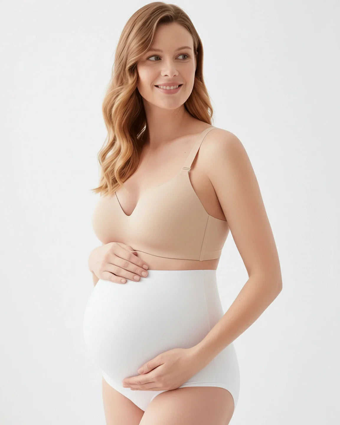 Smiling pregnant woman in a nude seamless maternity bra and white full-coverage high-waist briefs.