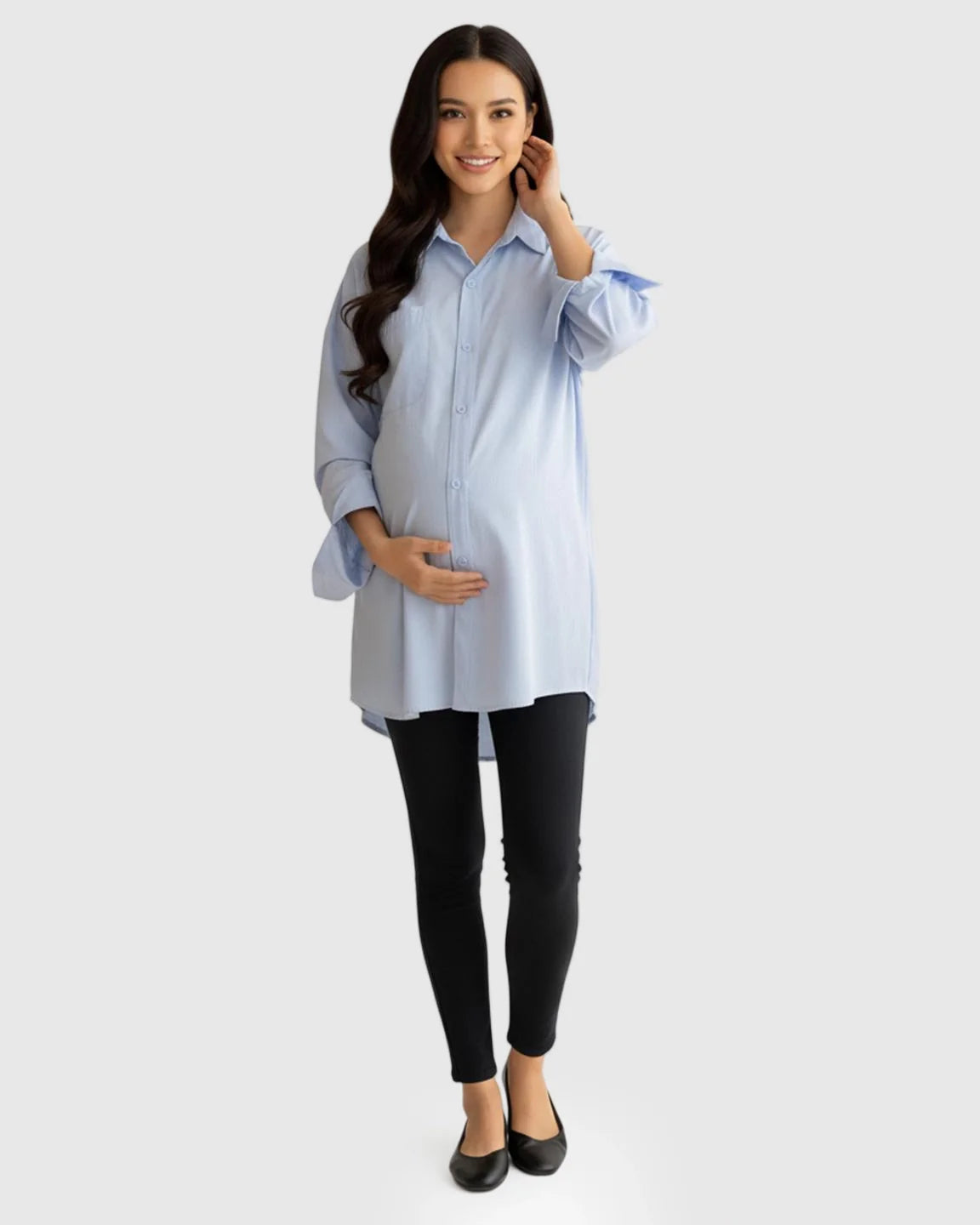 Smiling pregnant woman in a light blue cotton lapel-collar button-front maternity tunic and black leggings.