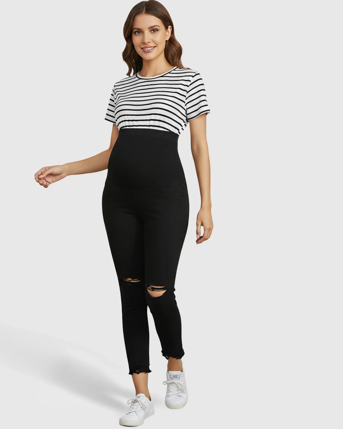 Smiling pregnant woman in black ripped maternity skinny jeans with an over-belly support panel and a striped top.