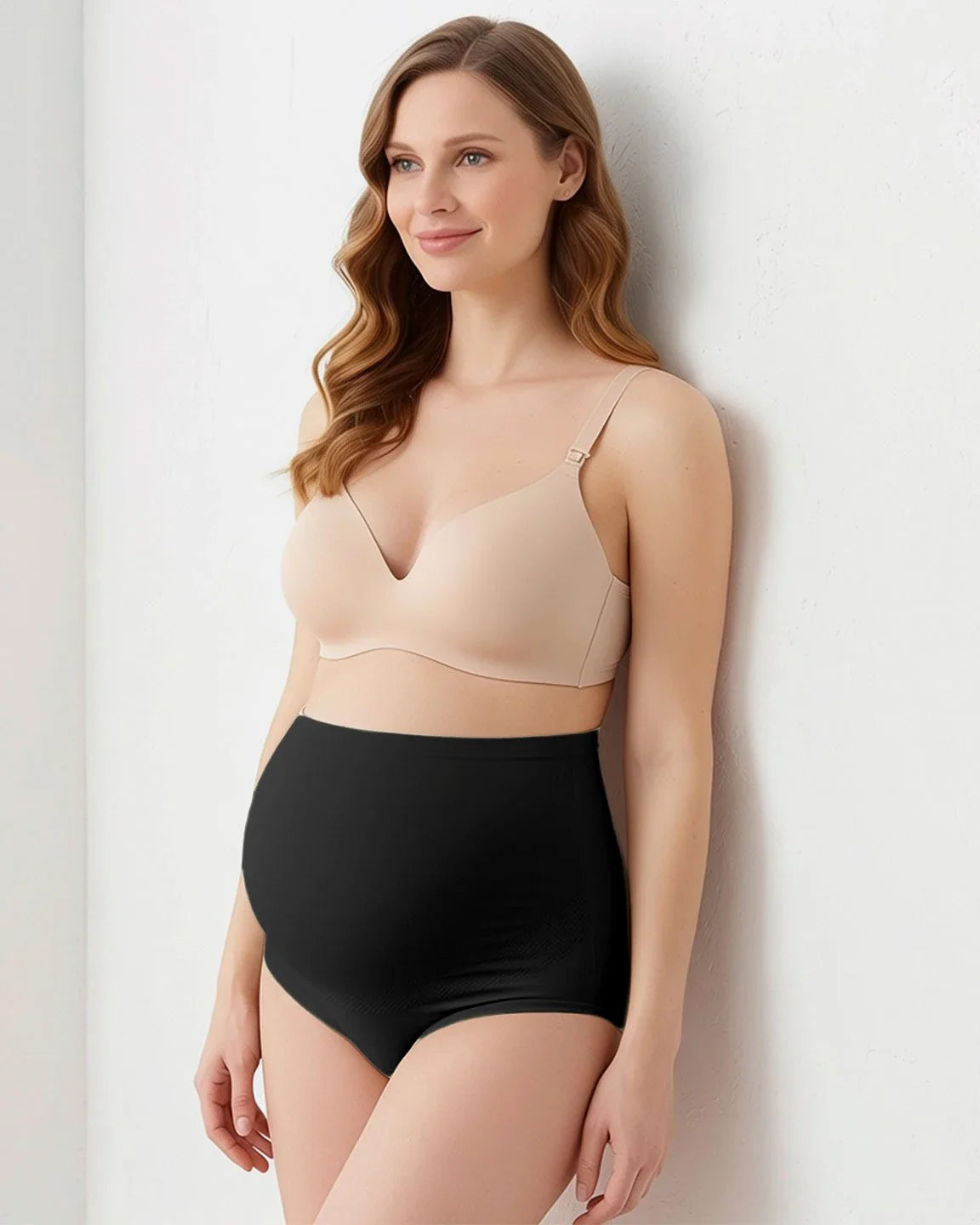 Smiling pregnant woman in black full-coverage seamless maternity briefs and a nude bra.