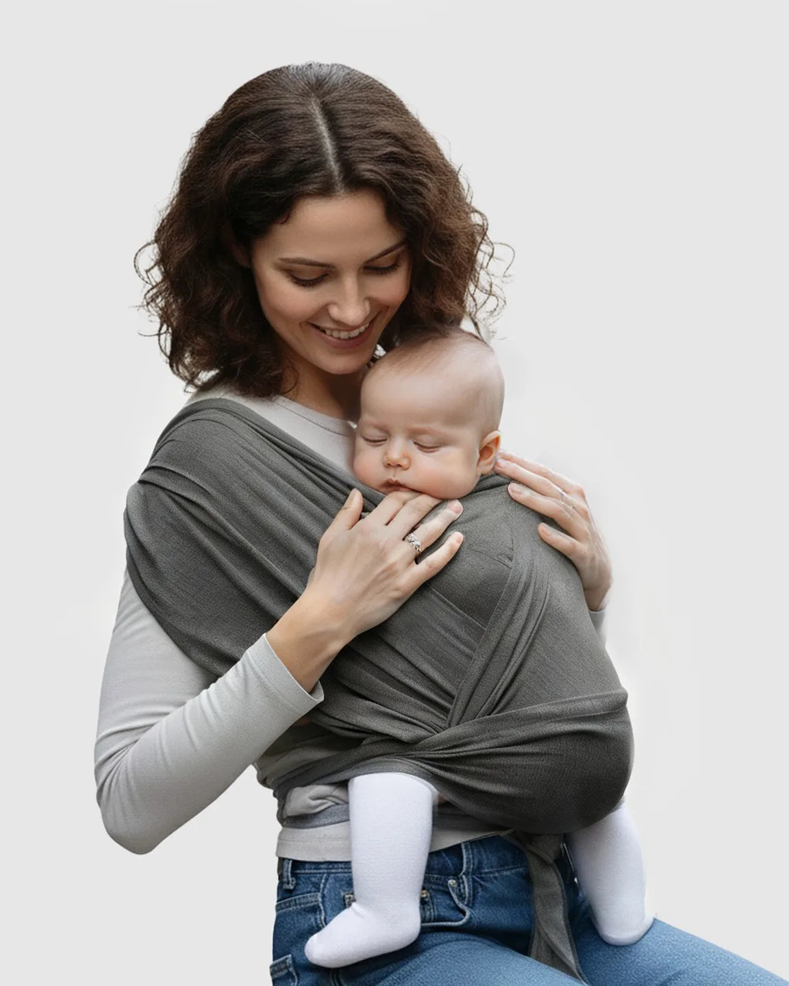 Smiling mom wearing a dark gray adjustable wrap-around baby carrier with a sleeping infant.
