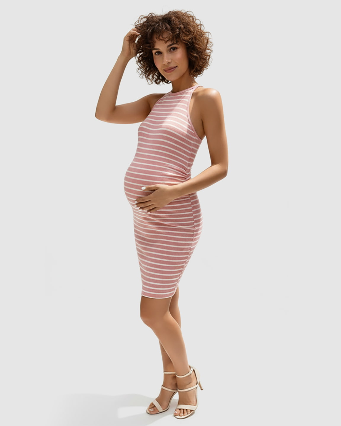 Pregnant woman in a pink and white striped halter bodycon maternity mini dress, holding her bump.