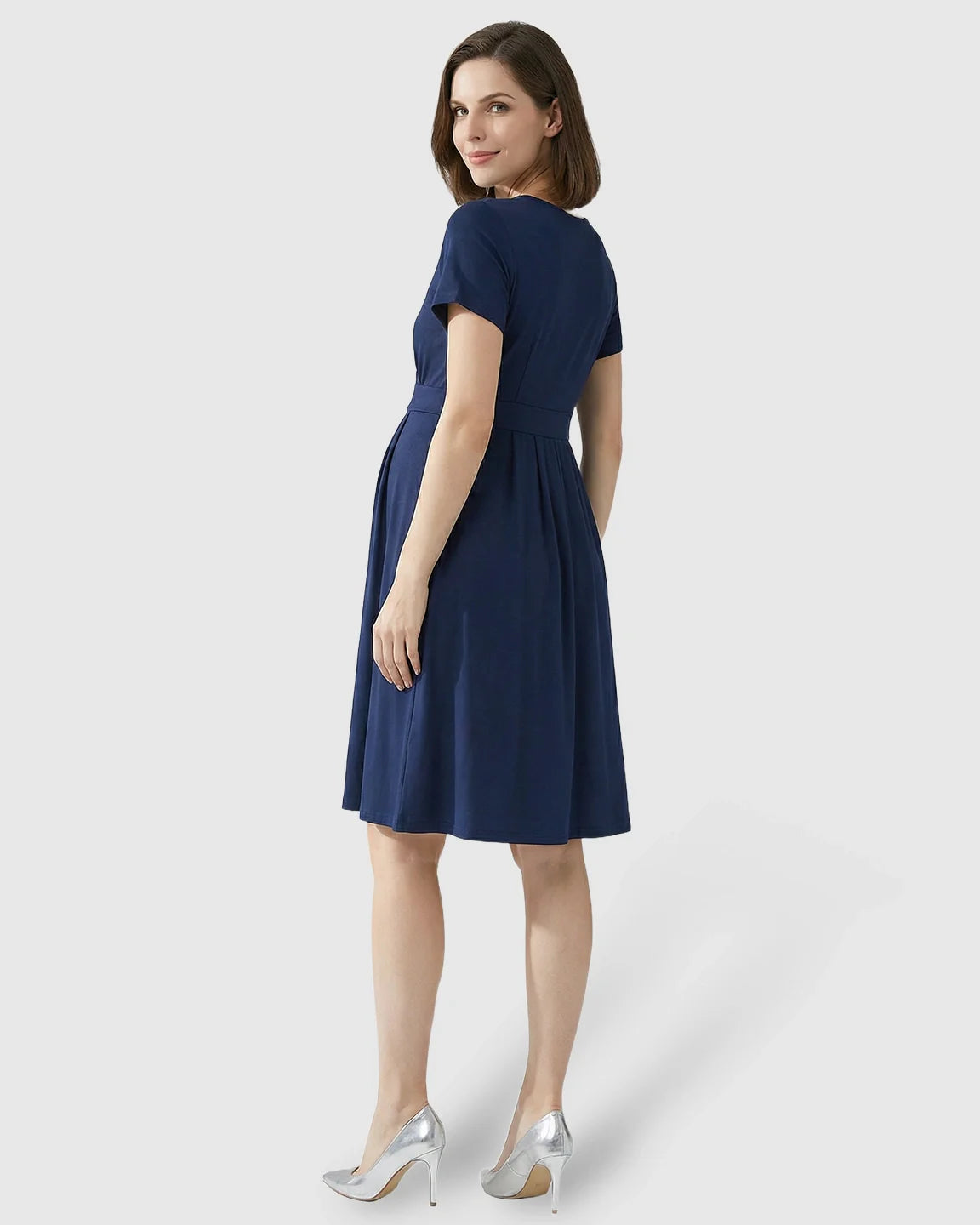 Woman in a navy V-neck A-line maternity and nursing dress with short sleeves, looking over her shoulder.