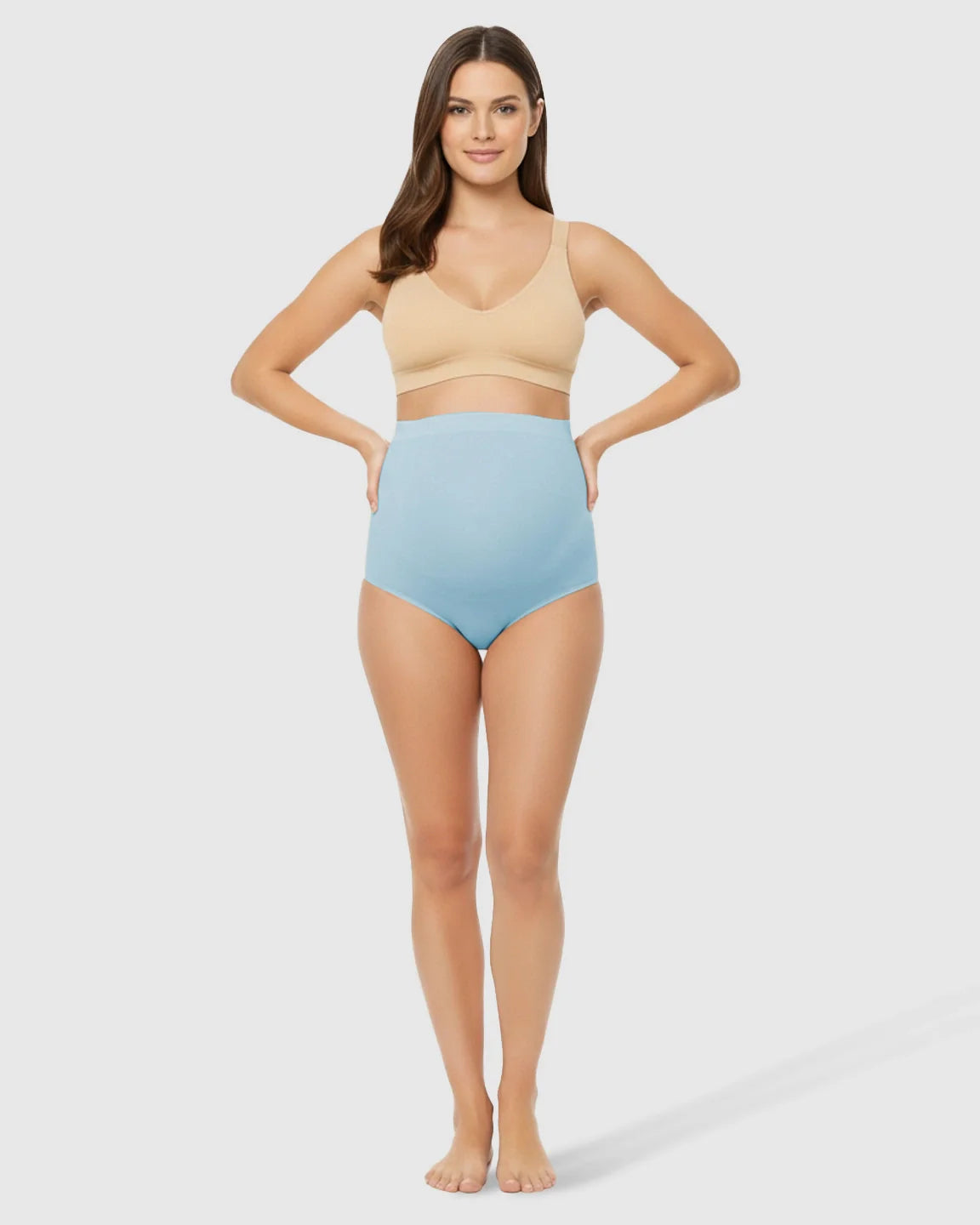 Smiling woman models light blue high-waist seamless belly-support maternity underwear with a nude bra.