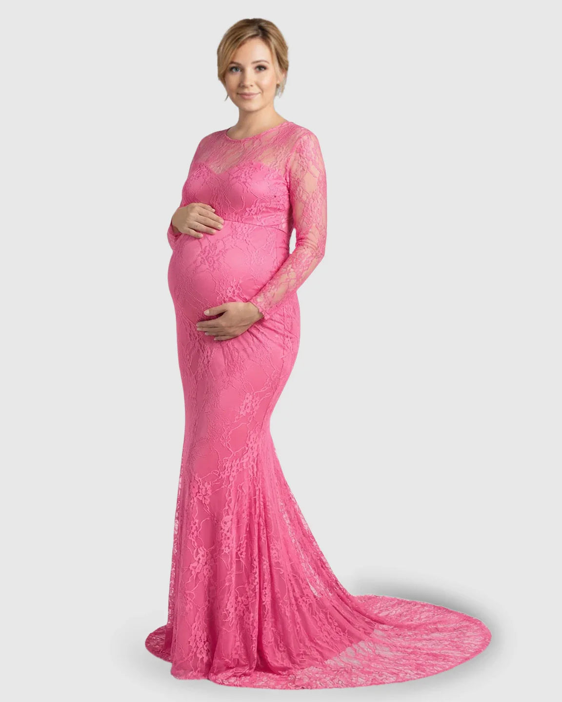 Pregnant woman in a pink sheer lace trumpet maternity photoshoot gown with long sleeves and a mermaid skirt.
