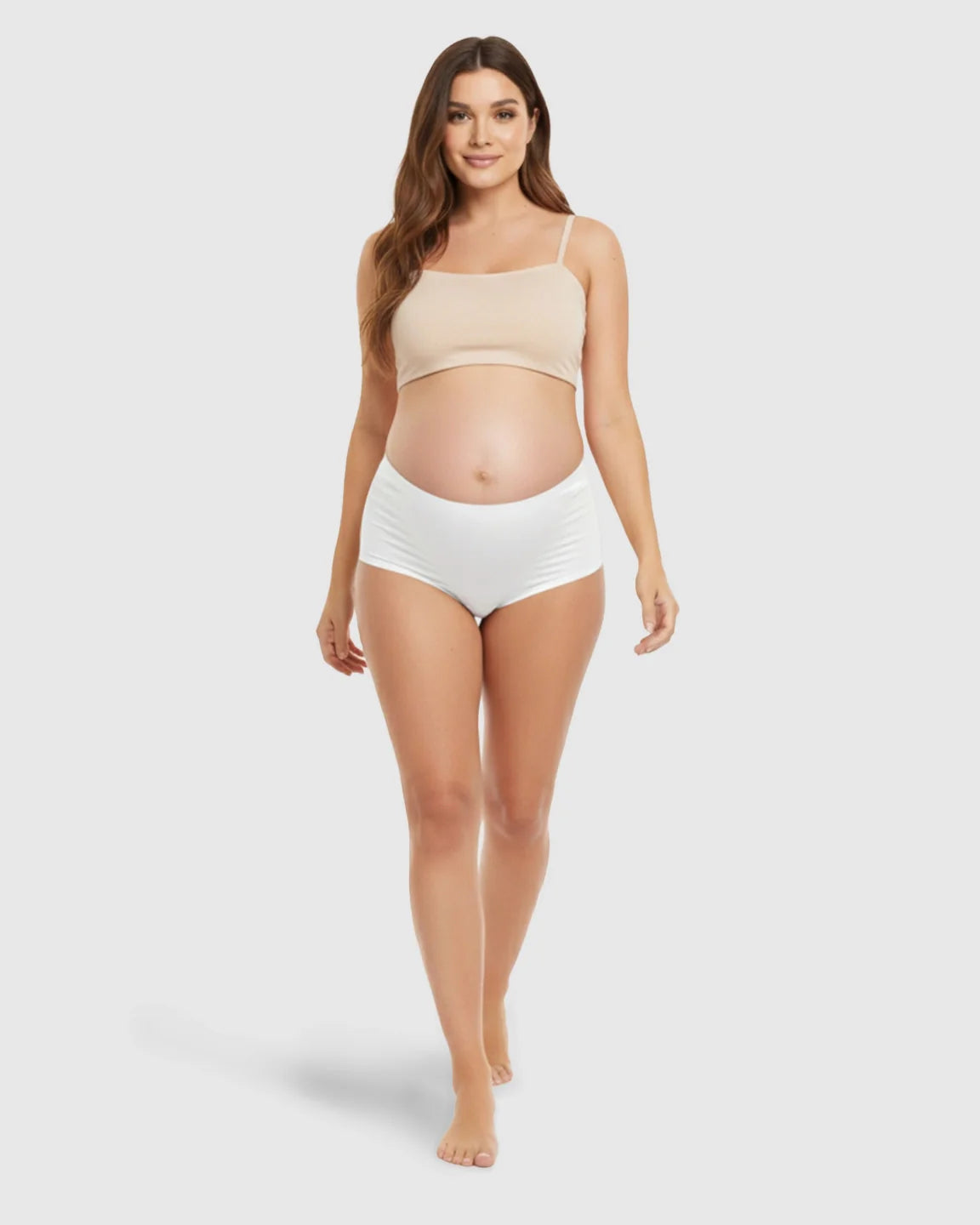 Smiling pregnant woman wearing a beige seamless maternity bra and white high-waist support underwear.