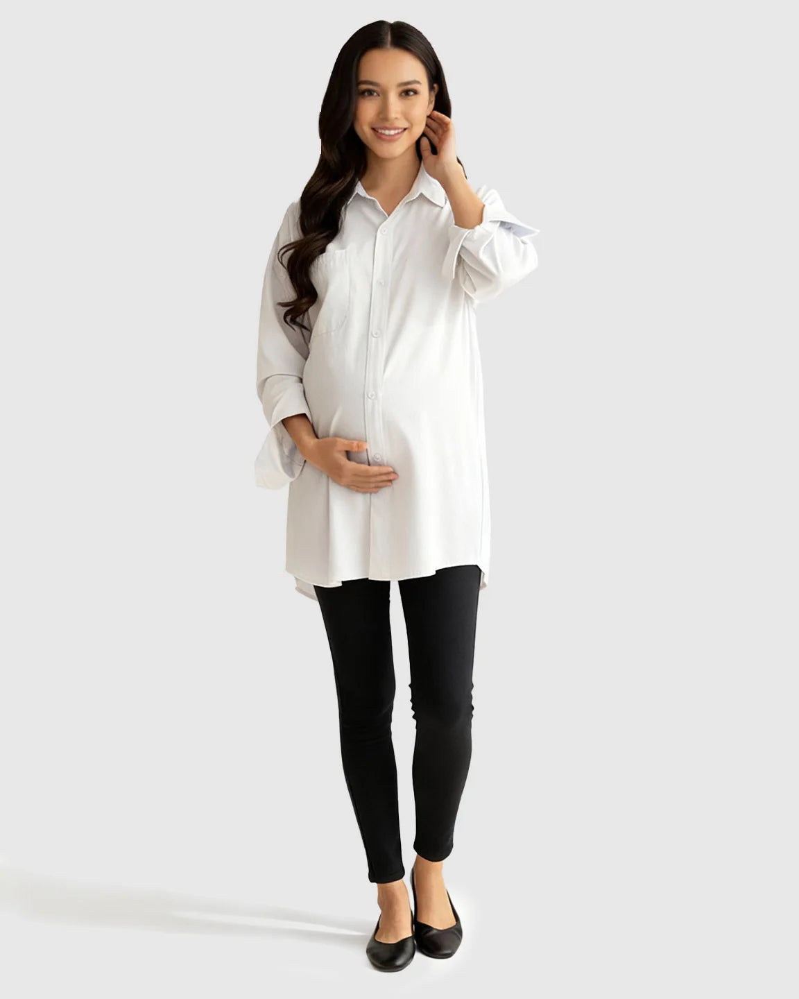 Smiling pregnant woman in a white cotton lapel-collar button-front maternity tunic and black leggings.