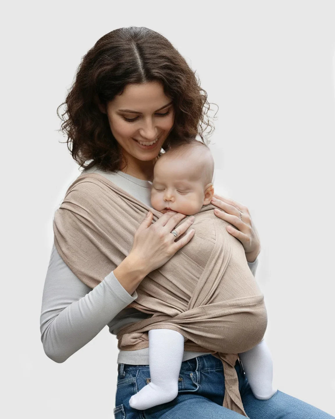 Smiling mom wearing a soft, beige adjustable wrap-around baby carrier with a sleeping infant.