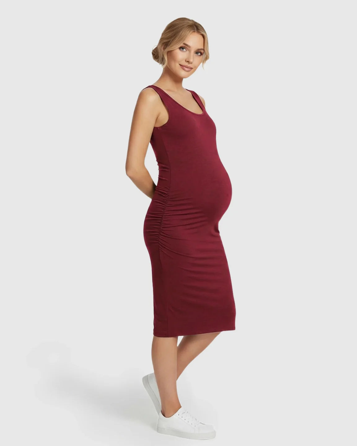 Pregnant woman in a sleeveless, dark red bodycon maternity dress with side ruching and white sneakers.