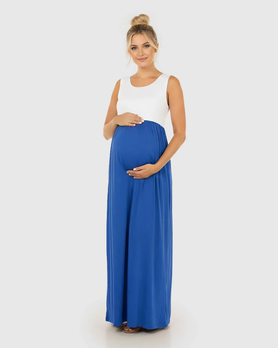 Smiling pregnant woman in a white and blue colorblock high-waisted maternity maxi dress, hands on bump.