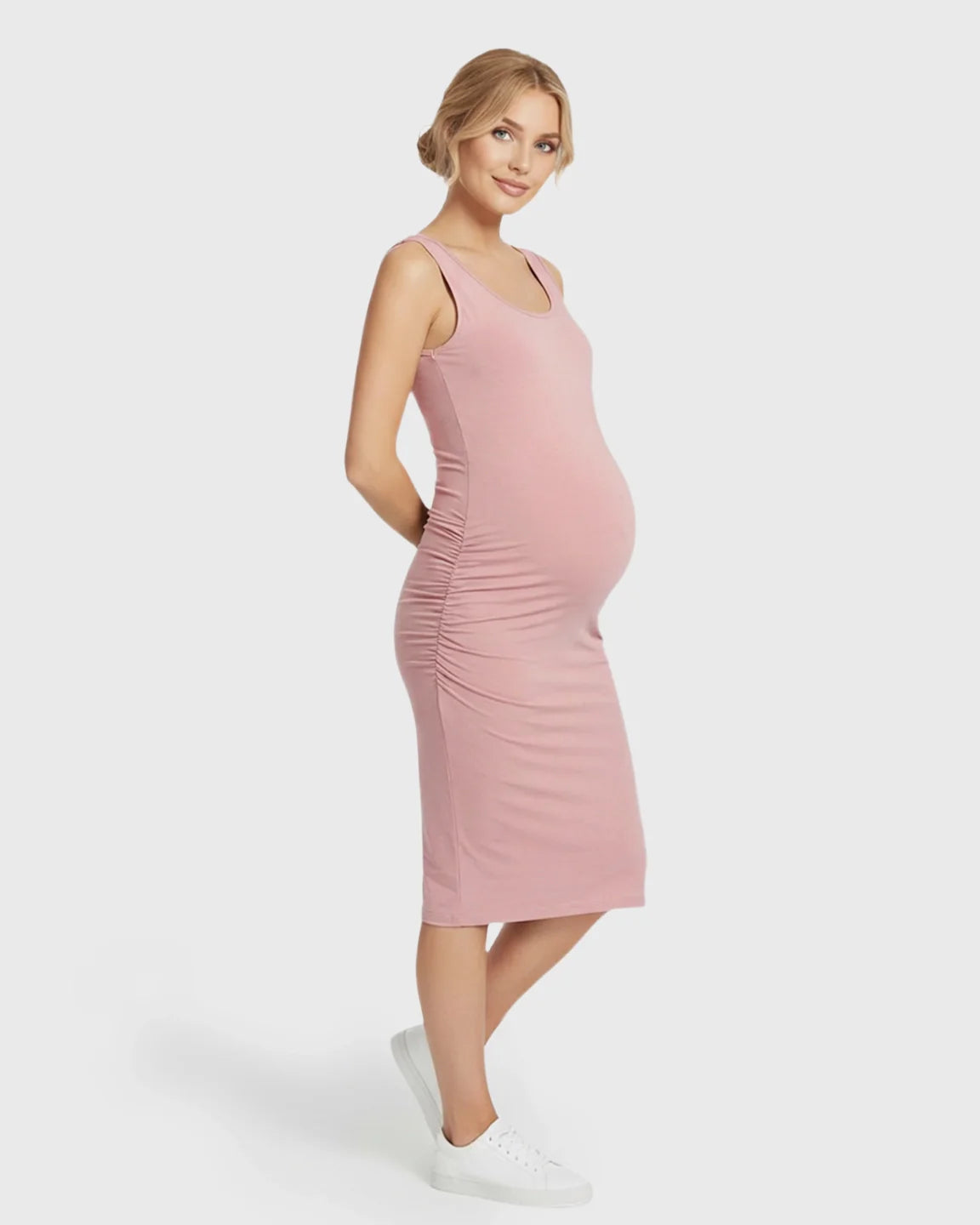 Blonde pregnant woman in a pink sleeveless bodycon maternity dress with side ruching, wearing white sneakers.