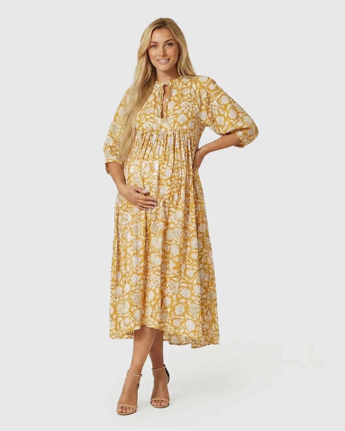 Pregnant woman in a yellow and white floral maternity midi dress with gathered shoulders and puff sleeves.