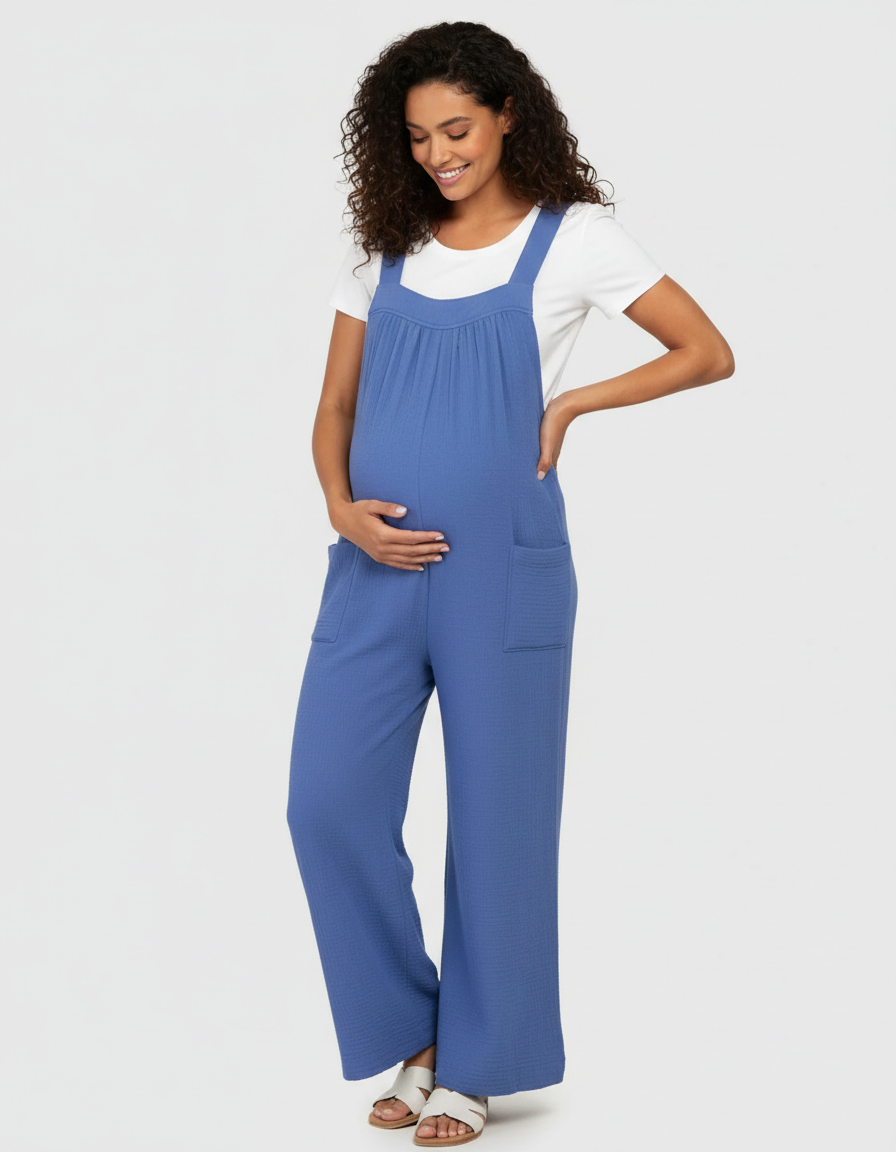 Smiling pregnant woman in a blue wide-leg maternity jumpsuit with a white tee, hands on belly.