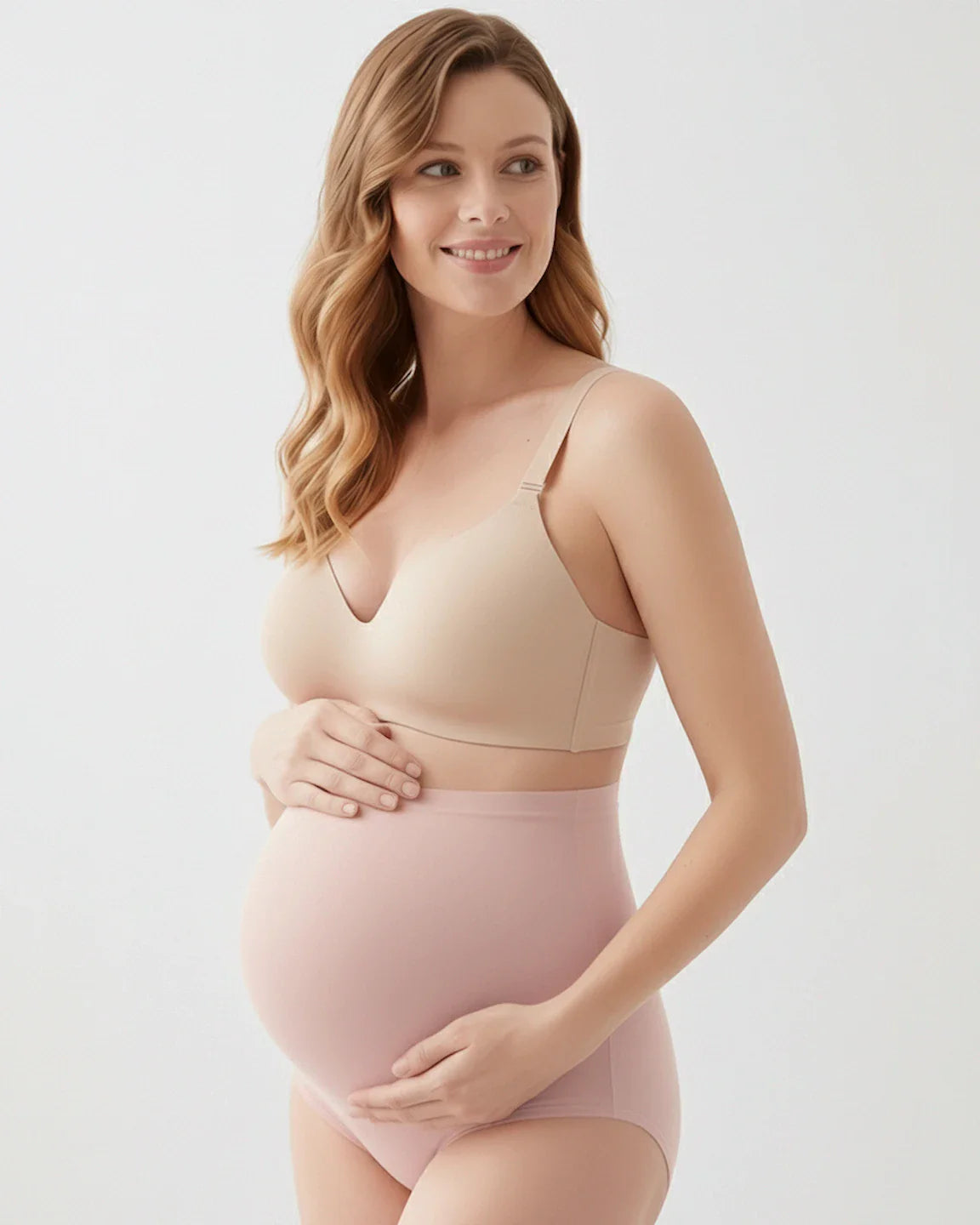 Smiling pregnant woman in a nude seamless maternity bra and pink full-coverage high-waist briefs.