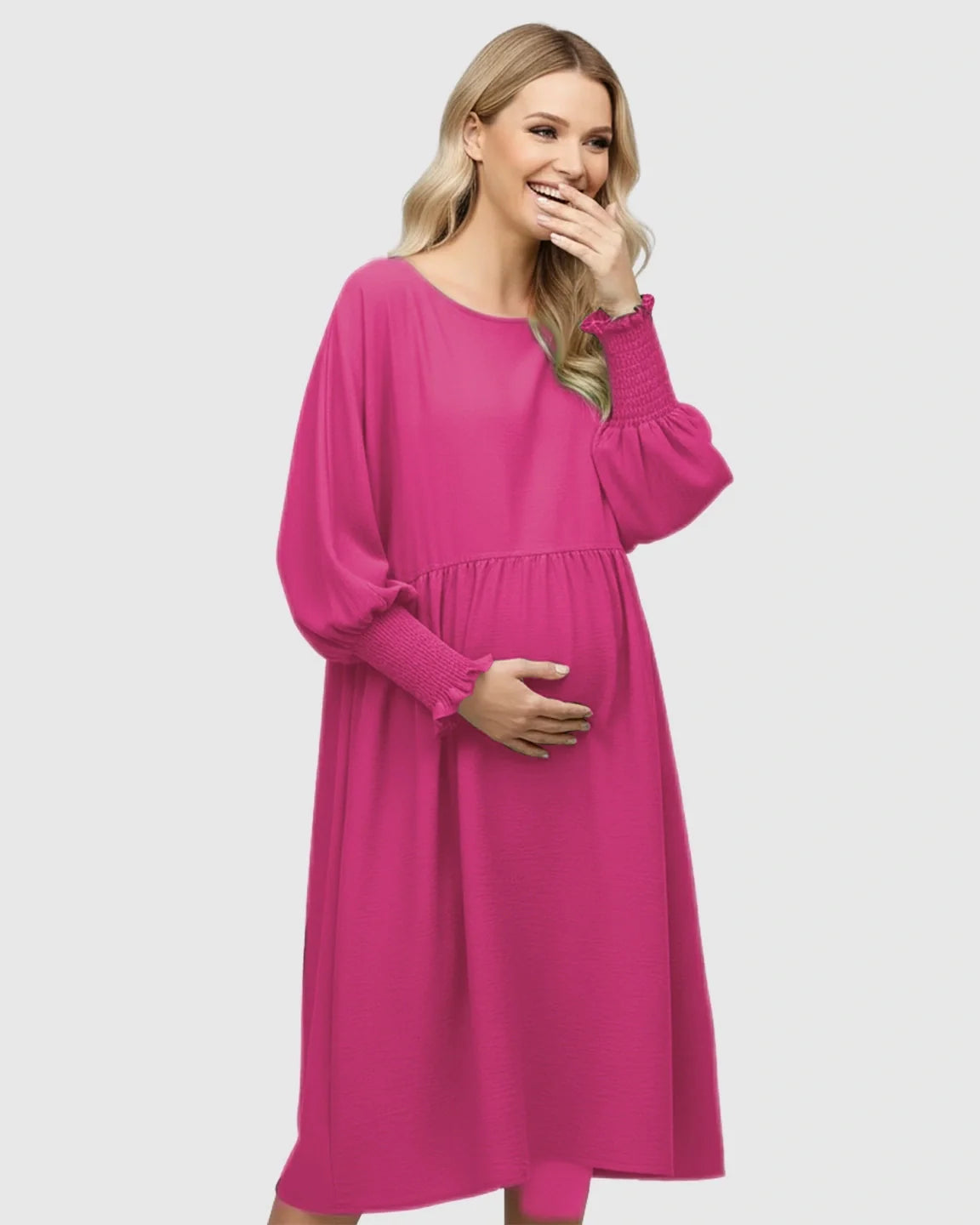 Smiling pregnant woman in a fuchsia smocked sleeve casual dress with a round neckline and flowing skirt.