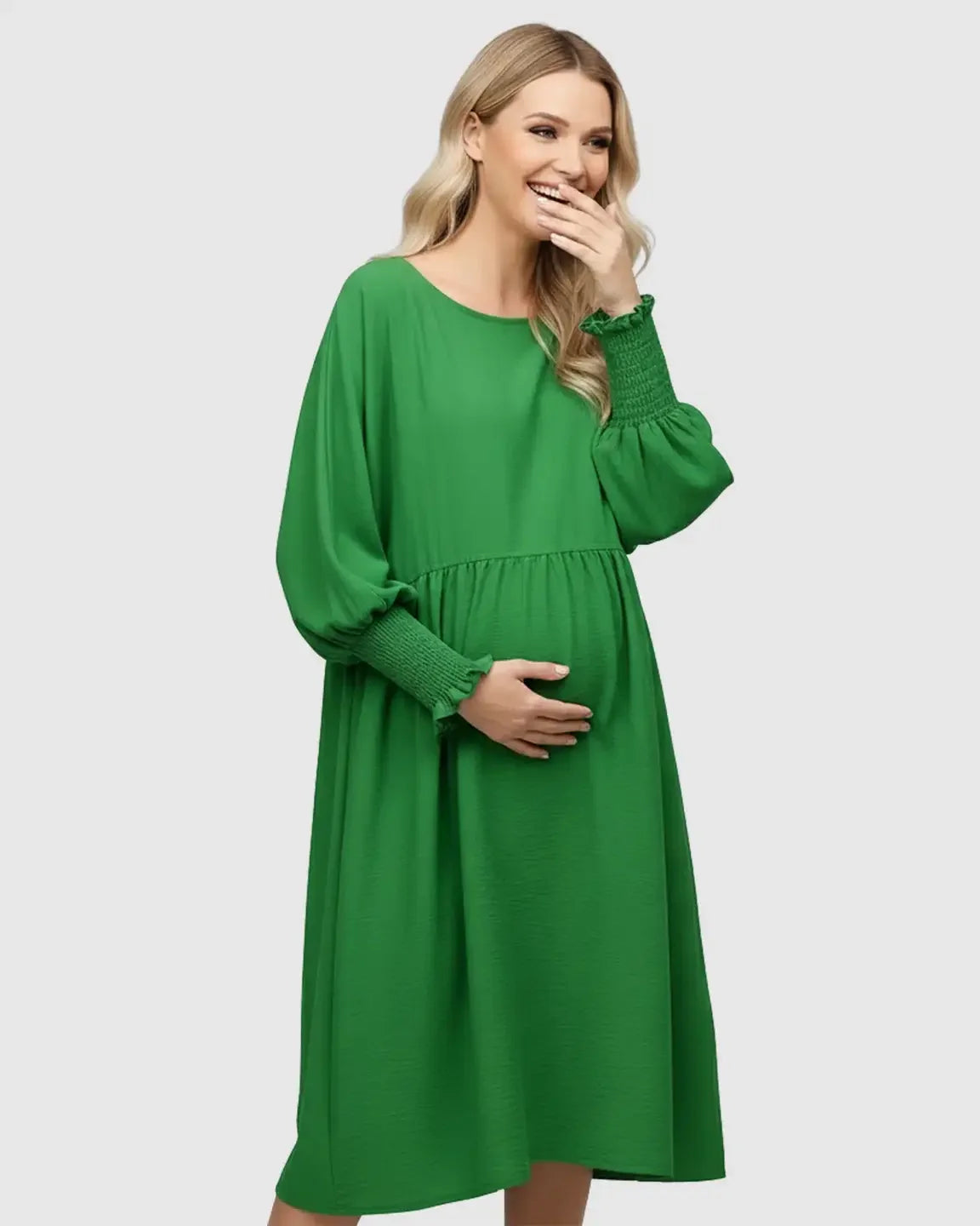 Smiling pregnant woman in a green smocked sleeve casual dress, holding her belly.