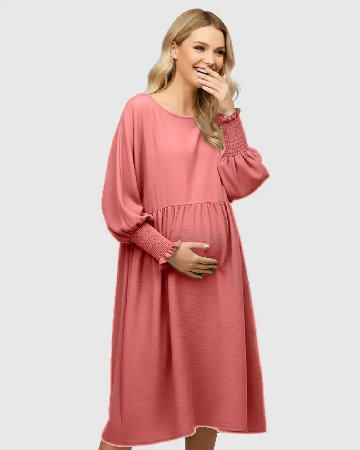 Smiling pregnant woman in a pink smocked sleeve casual maternity dress, holding her belly.