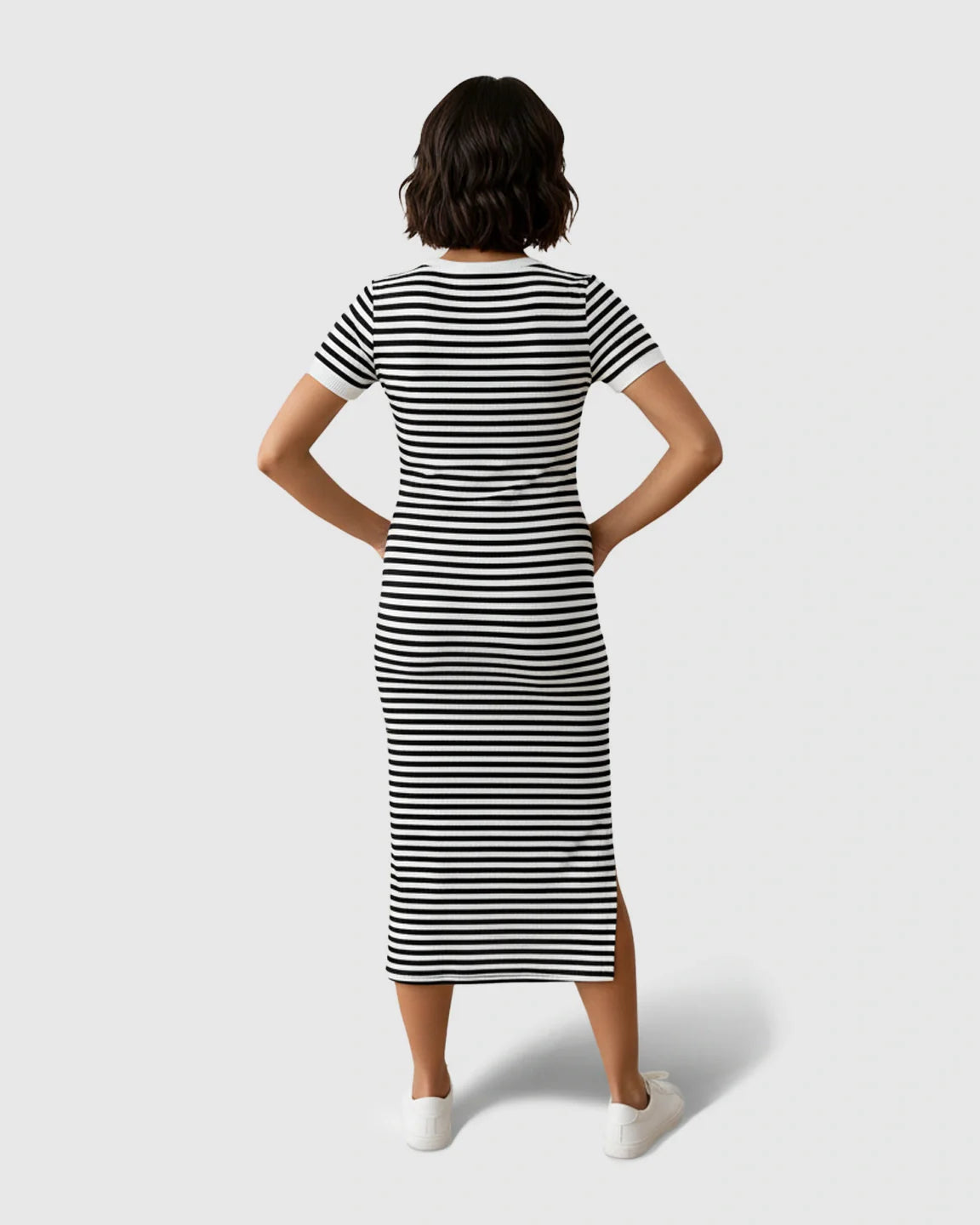 Woman from behind in a black and white striped maternity column dress with short sleeves and a side slit.