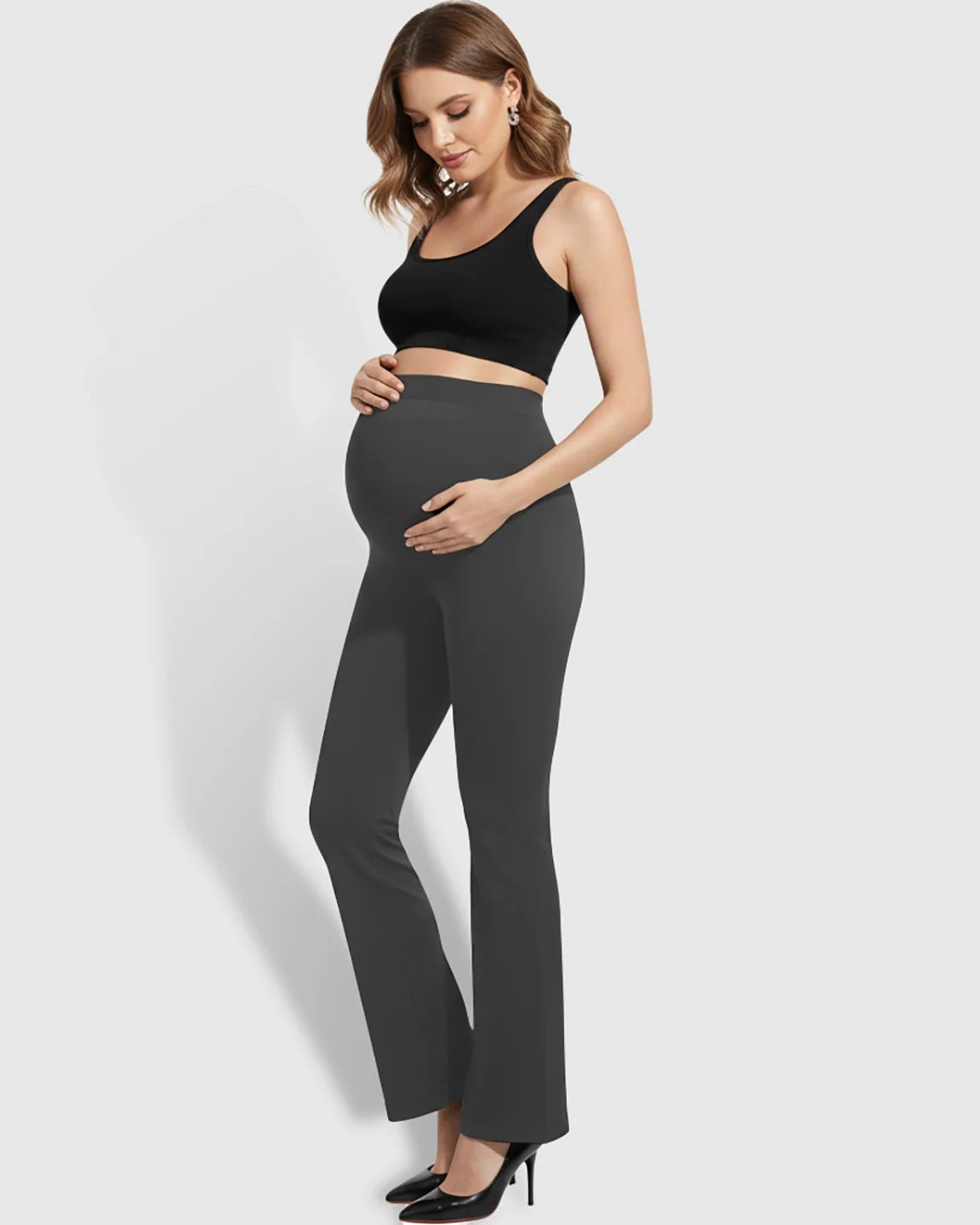 Pregnant woman wearing dark gray over-belly bootcut maternity pants with a soft flare.