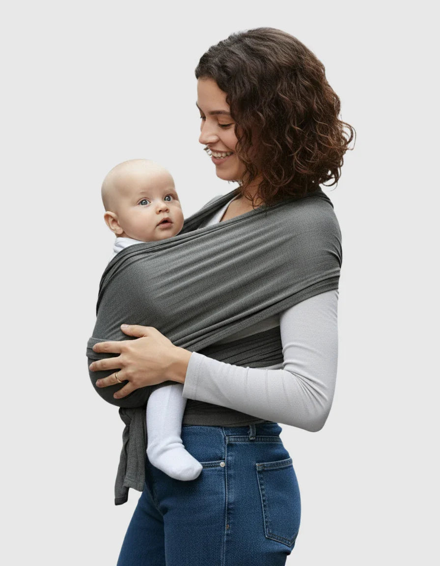 Smiling woman wearing a dark gray adjustable wrap-around baby carrier with a baby nestled inside.