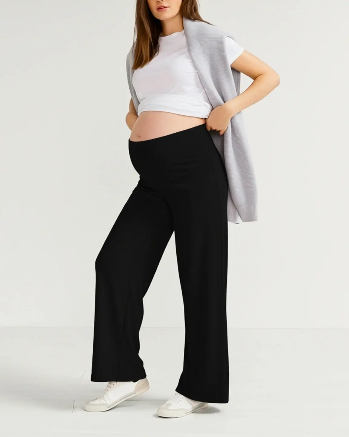 Pregnant woman in black wide-leg stretch maternity pants with an over-bump waistband, white tee, and gray sweater.