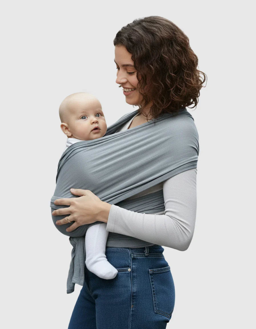 Smiling woman wearing a soft gray adjustable wrap-around baby carrier with a baby nestled inside.