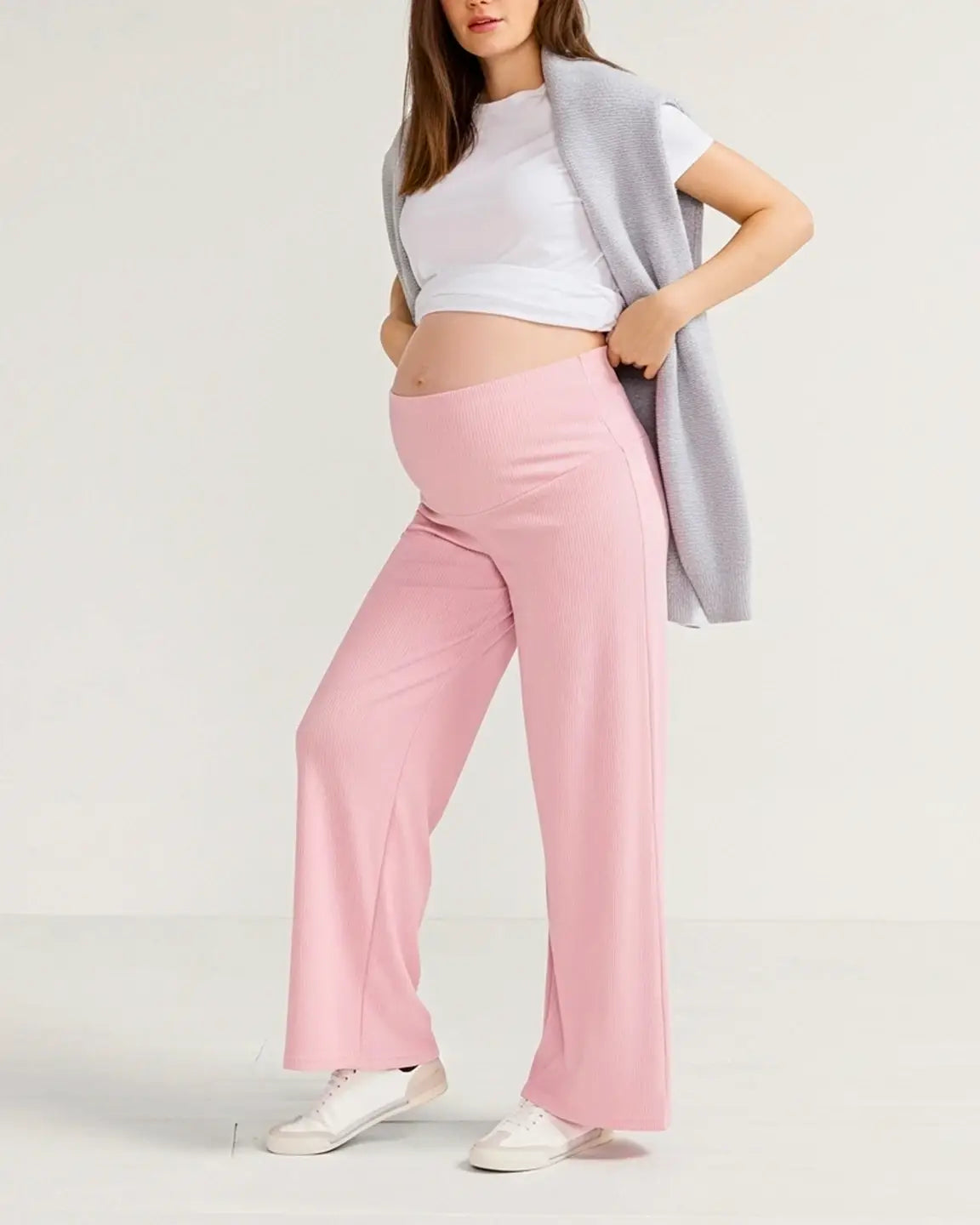 Woman wearing pink ribbed wide-leg maternity pants with an over-the-belly waistband and white sneakers.
