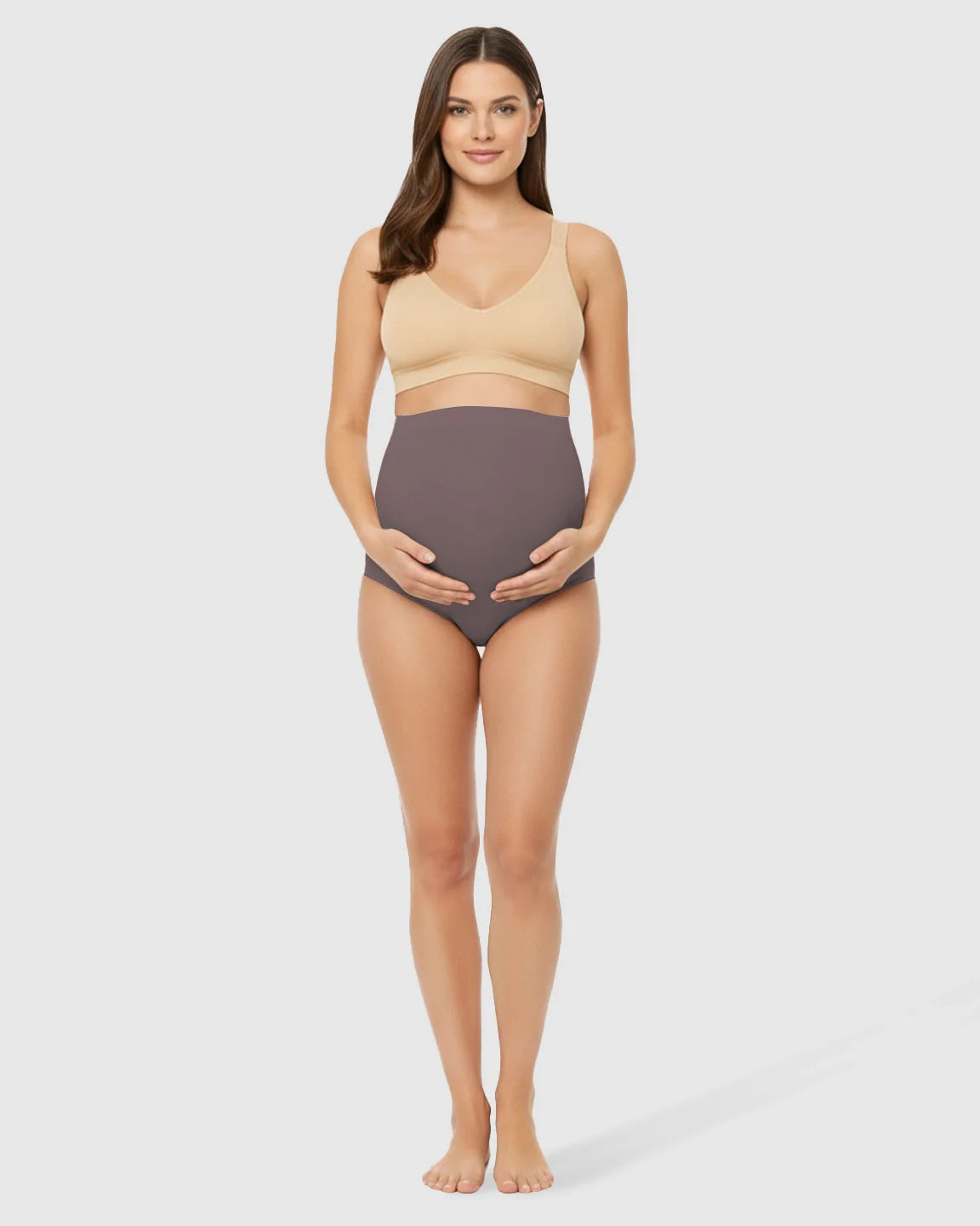 Pregnant woman in seamless high-waist charcoal maternity underwear and a nude bra, cradling her belly.