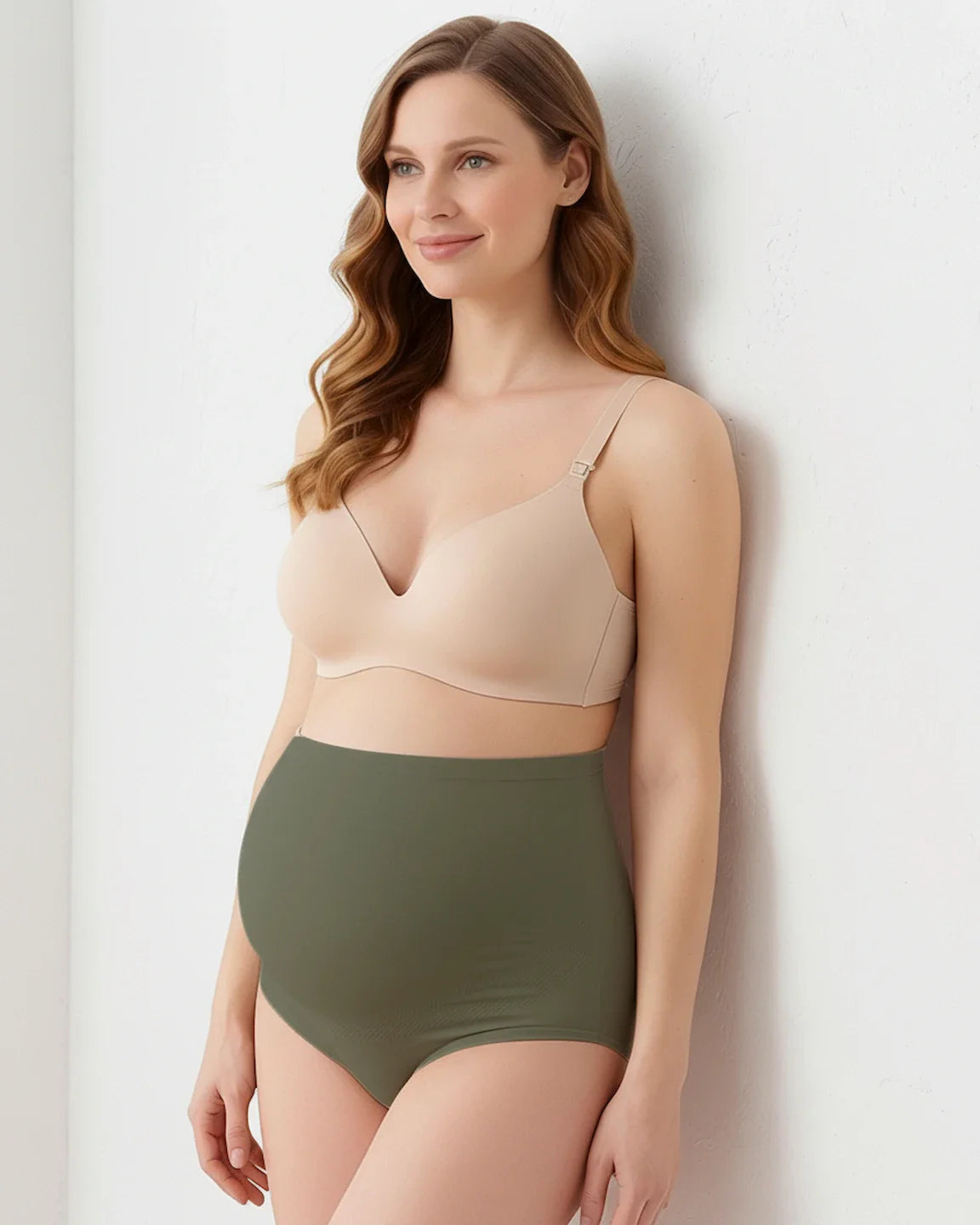 Smiling pregnant woman models olive green full-coverage seamless maternity briefs and a nude bra.